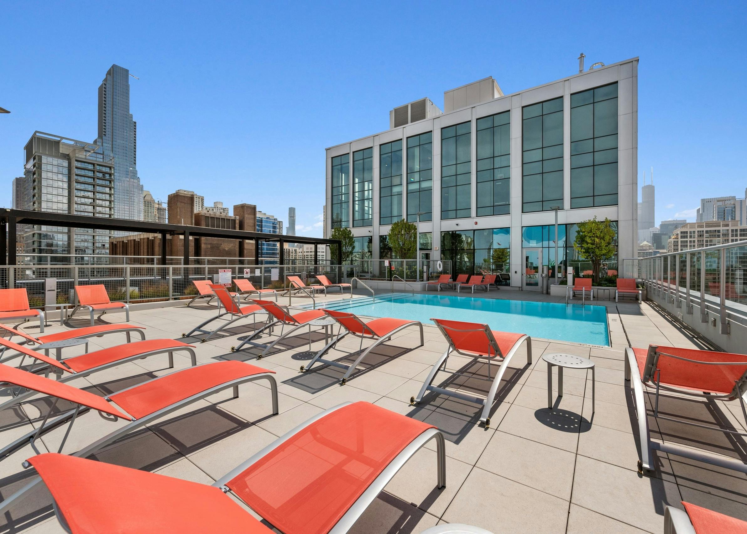 Luxurious rooftop pool at AMLI 808 apartment building with orange lounge chairs surrounded by stunning Chicago skyline views