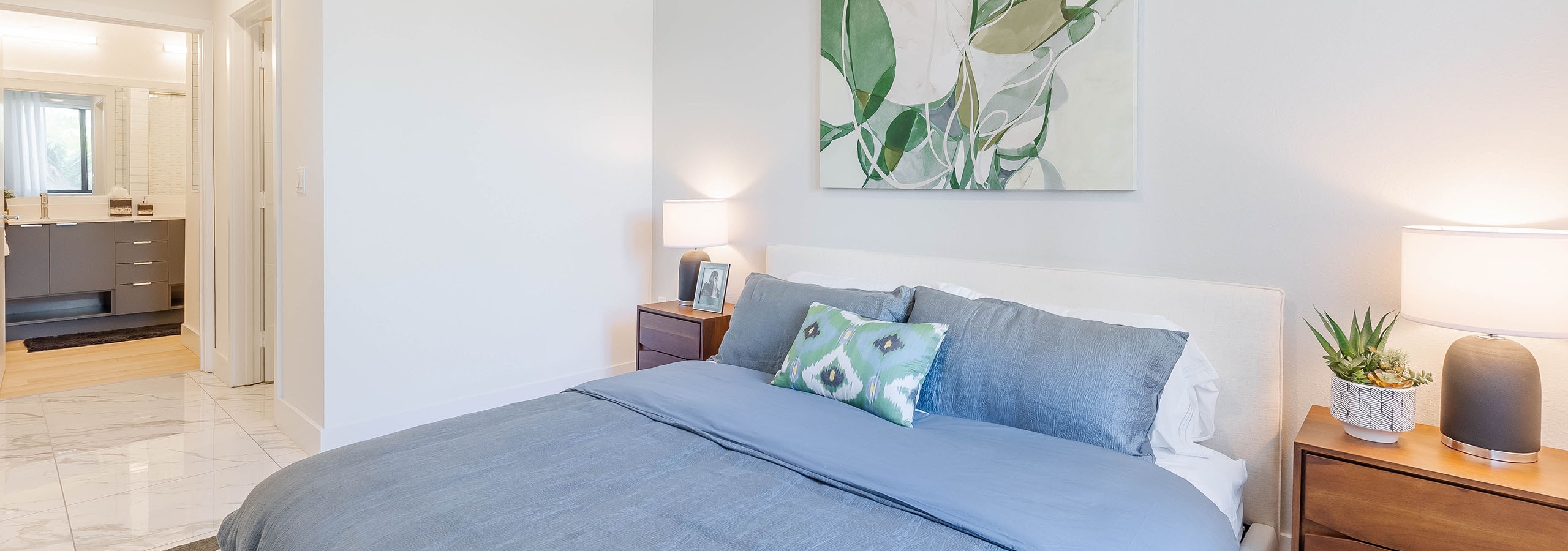 AMLI Park West apartment bedroom with gray bedding on low profile bed with two brown wood nightstands and view of bathroom