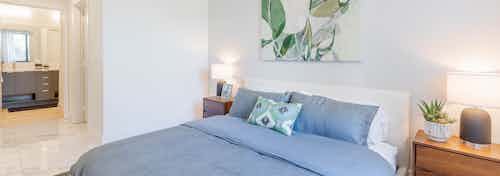 AMLI Park West apartment bedroom with gray bedding on low profile bed with two brown wood nightstands and view of bathroom