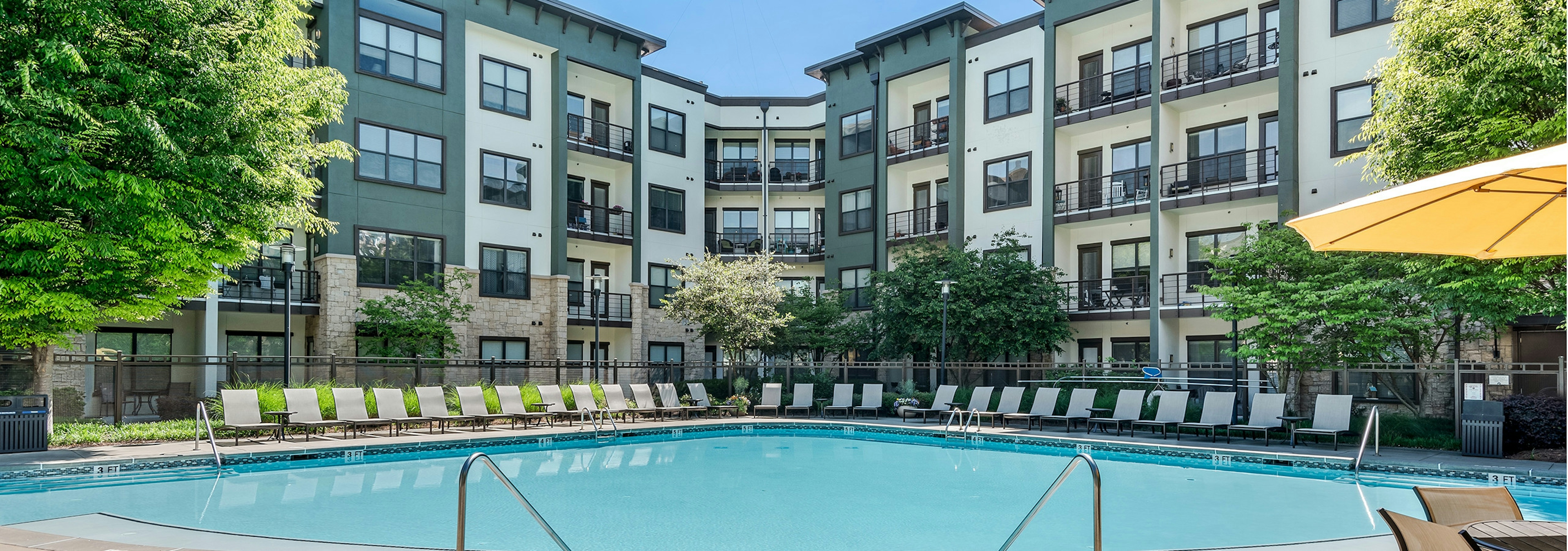 Exterior view of pool at AMLI Parkside surrounded by white lounge chairs with building straight ahead of it on a sunny day