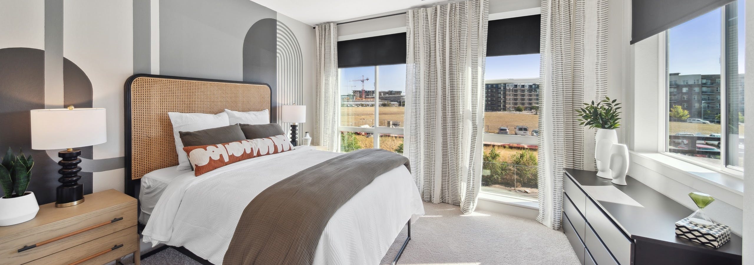 Bedroom at AMLI RiNo with gray geometric painted wall behind bed with white comforter and black dresser and 2 walls of windows