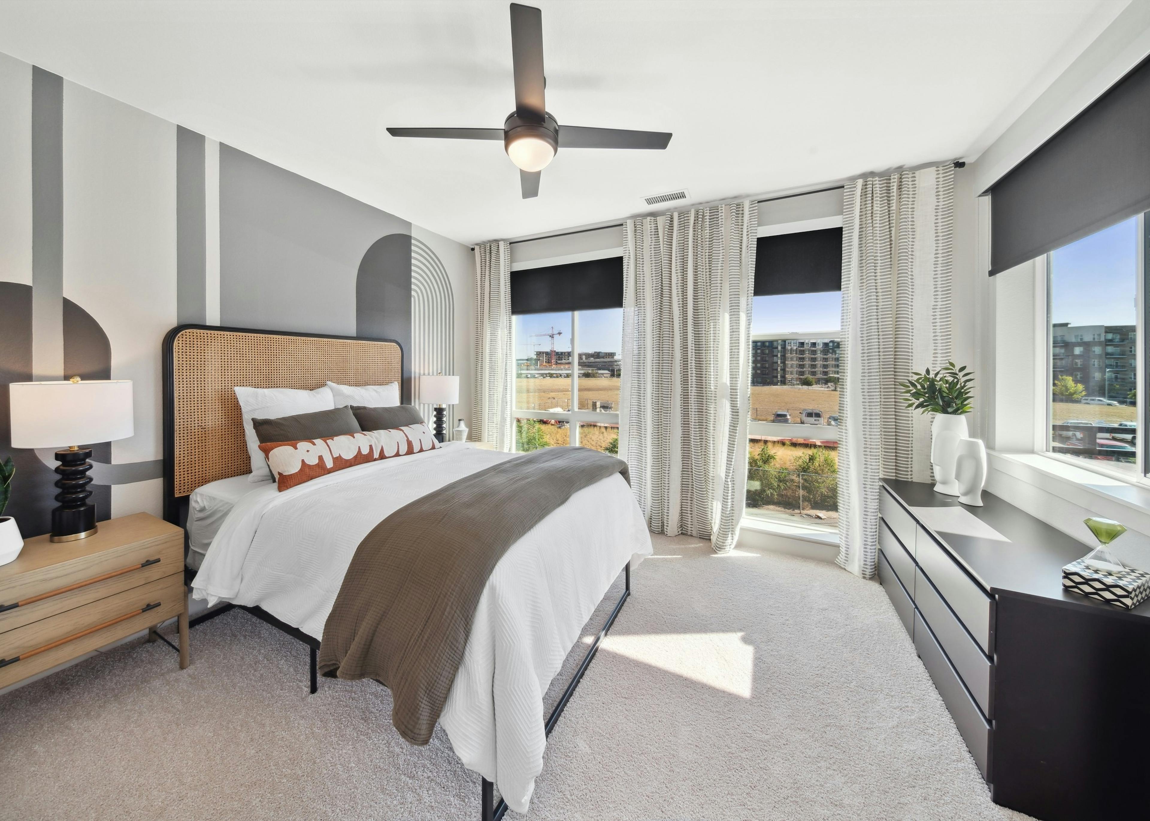 Bedroom at AMLI RiNo with gray geometric painted wall behind bed with white comforter and black dresser and 2 walls of windows