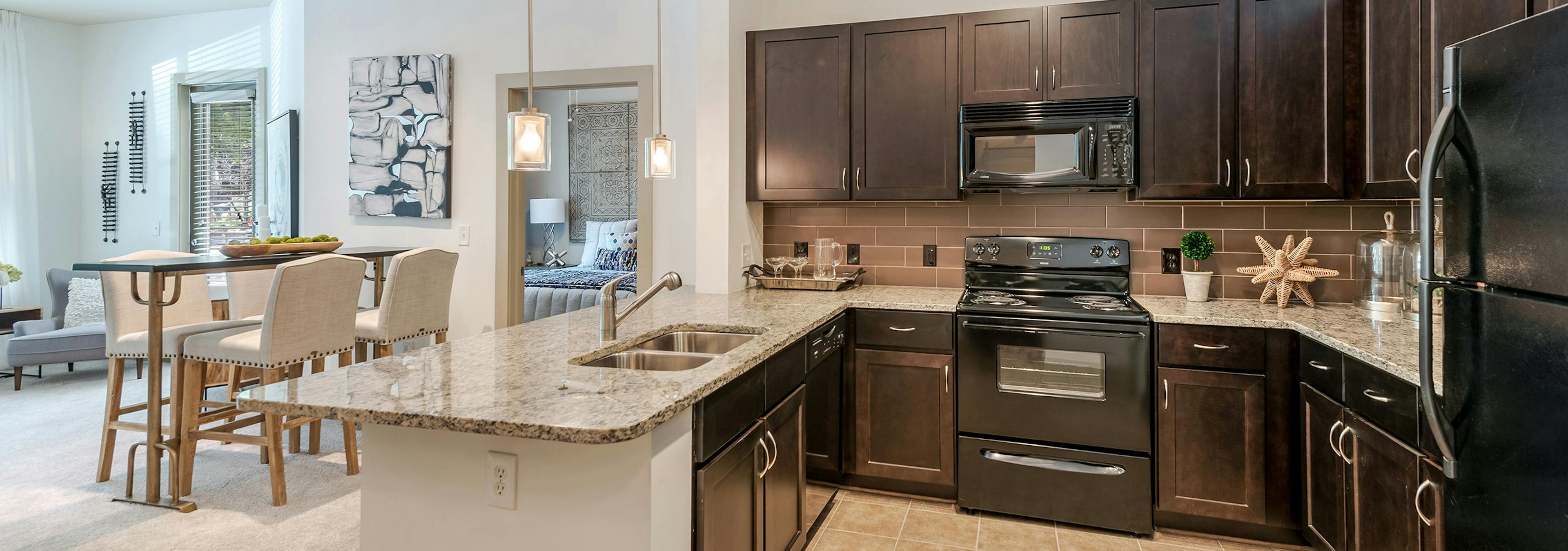 AMLI Parkside apartment spacious kitchen with light tile and dark cabinetry and black appliances with peek into living room