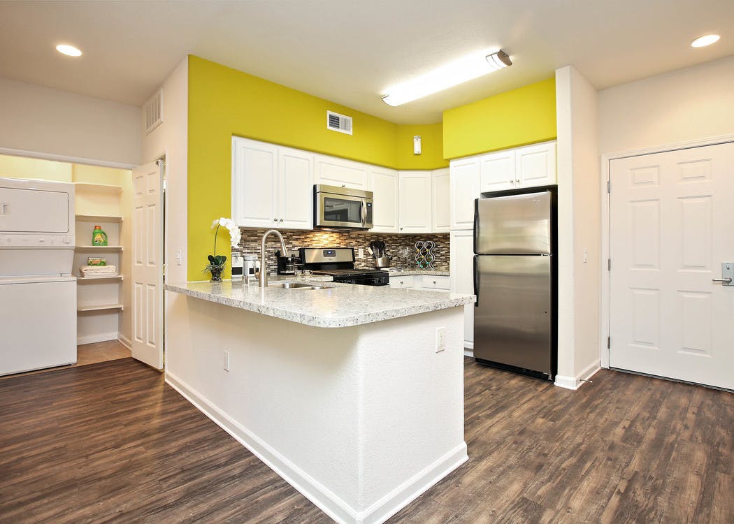 Interior of AMLI Warner Center apartment kitchen with white cabinetry, stainless steel appliances and peek into laundry area
