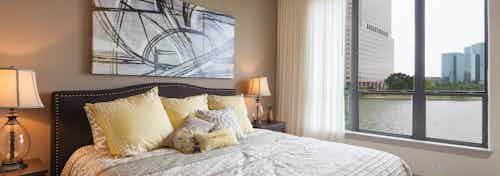 Interior view of AMLI Las Colinas apartment bedroom with bed and nightstands and large window with curtains overlooking lake