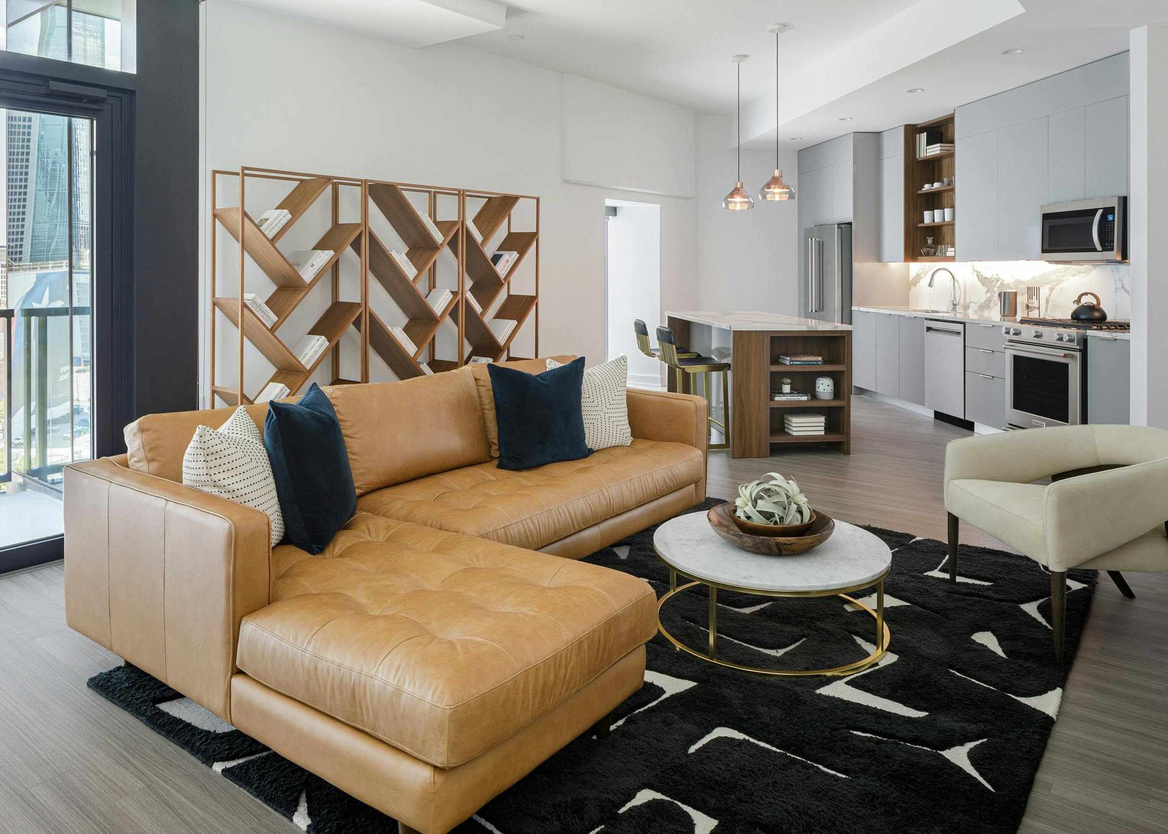Interior view of AMLI Fountain Place living room with large camel leather couch in center and gray island kitchen behind