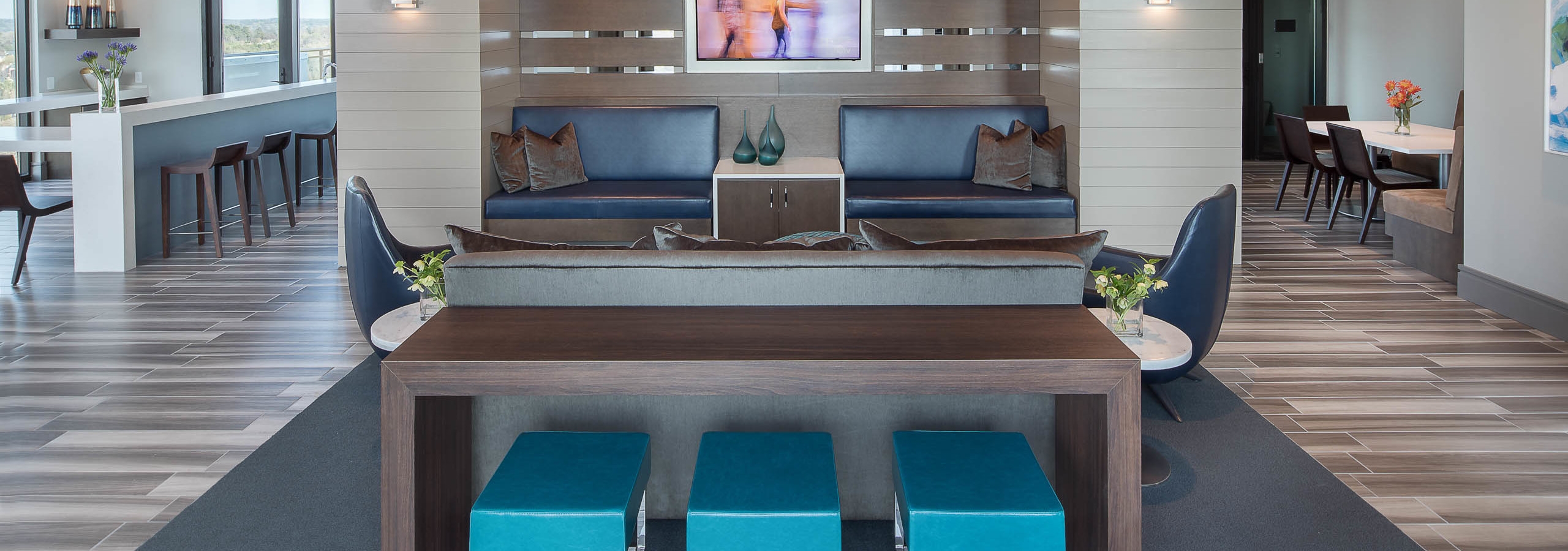 AMLI 3464 clubroom dark wood table in front of blue booth seats and a long white counter with barstools in the background