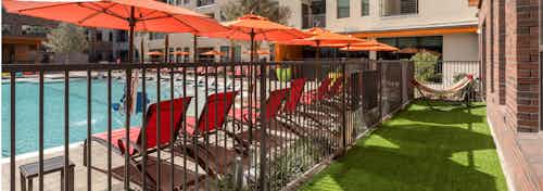 Close up view through black fence of lounge chairs under orange umbrellas in swimming pool area at AMLI on Aldrich