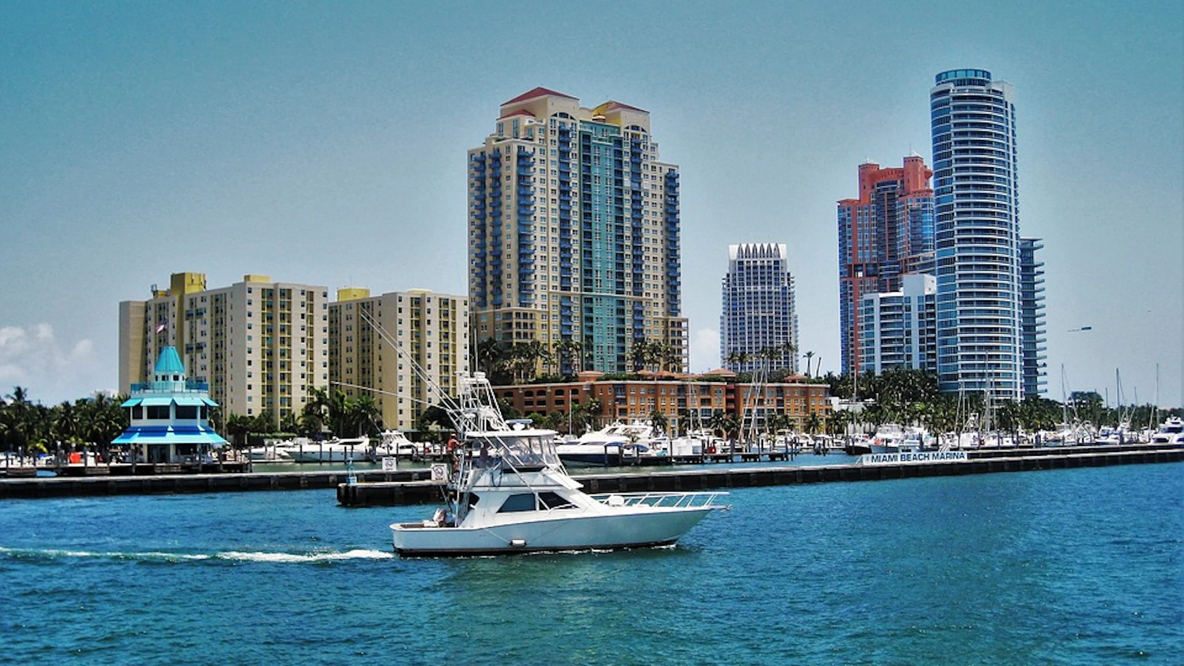 A yacht sailing across a bay in front of tall buildings of Miami Beach