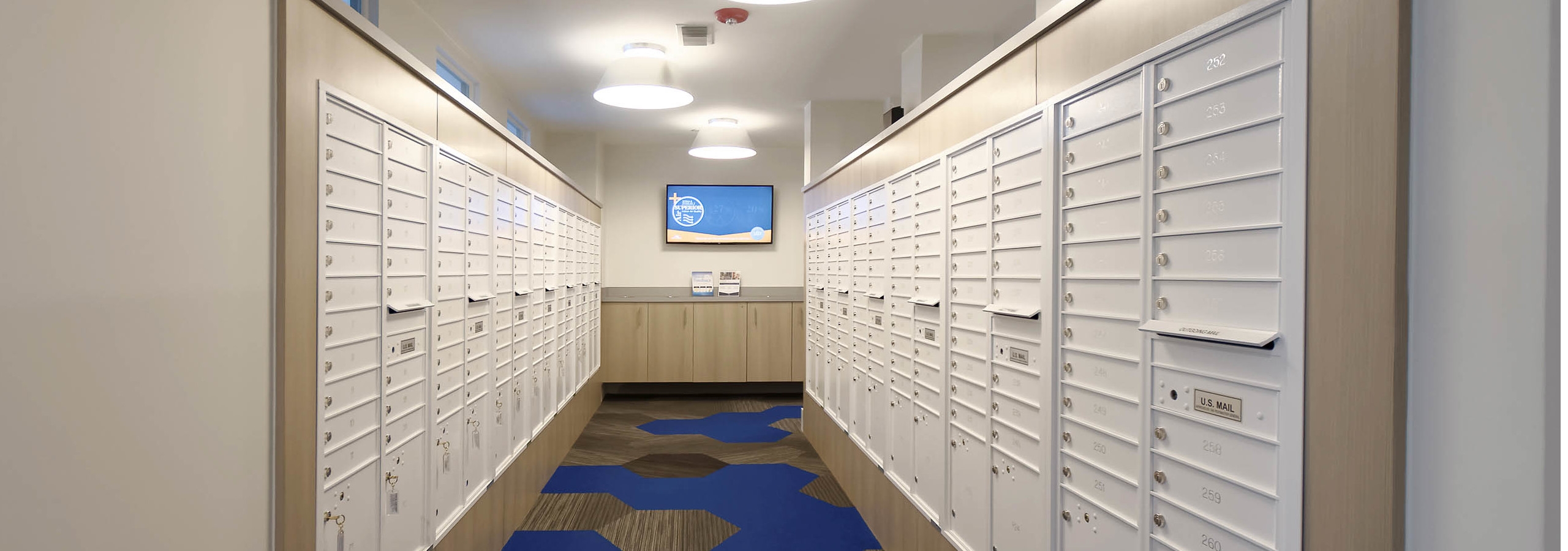 Interior view of the mail room at AMLI Dry Creek apartments with all resident mail boxes and carpeting and a television