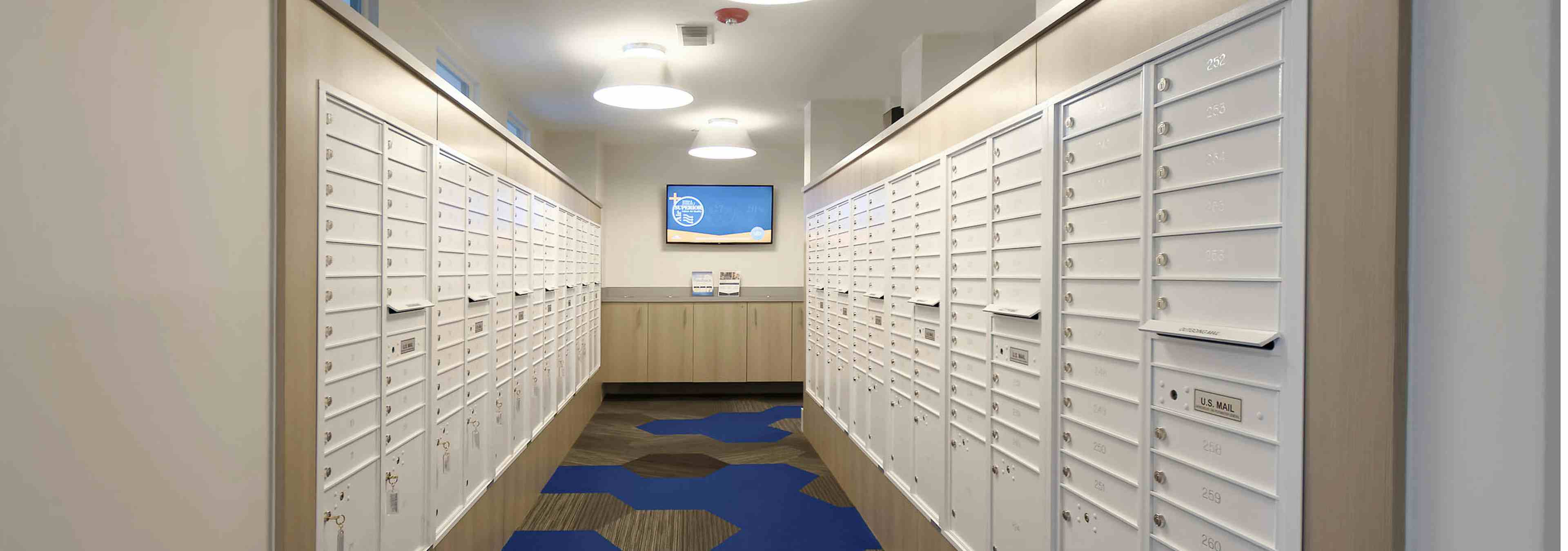 Interior view of the mail room at AMLI Dry Creek apartments with all resident mail boxes and carpeting and a television 