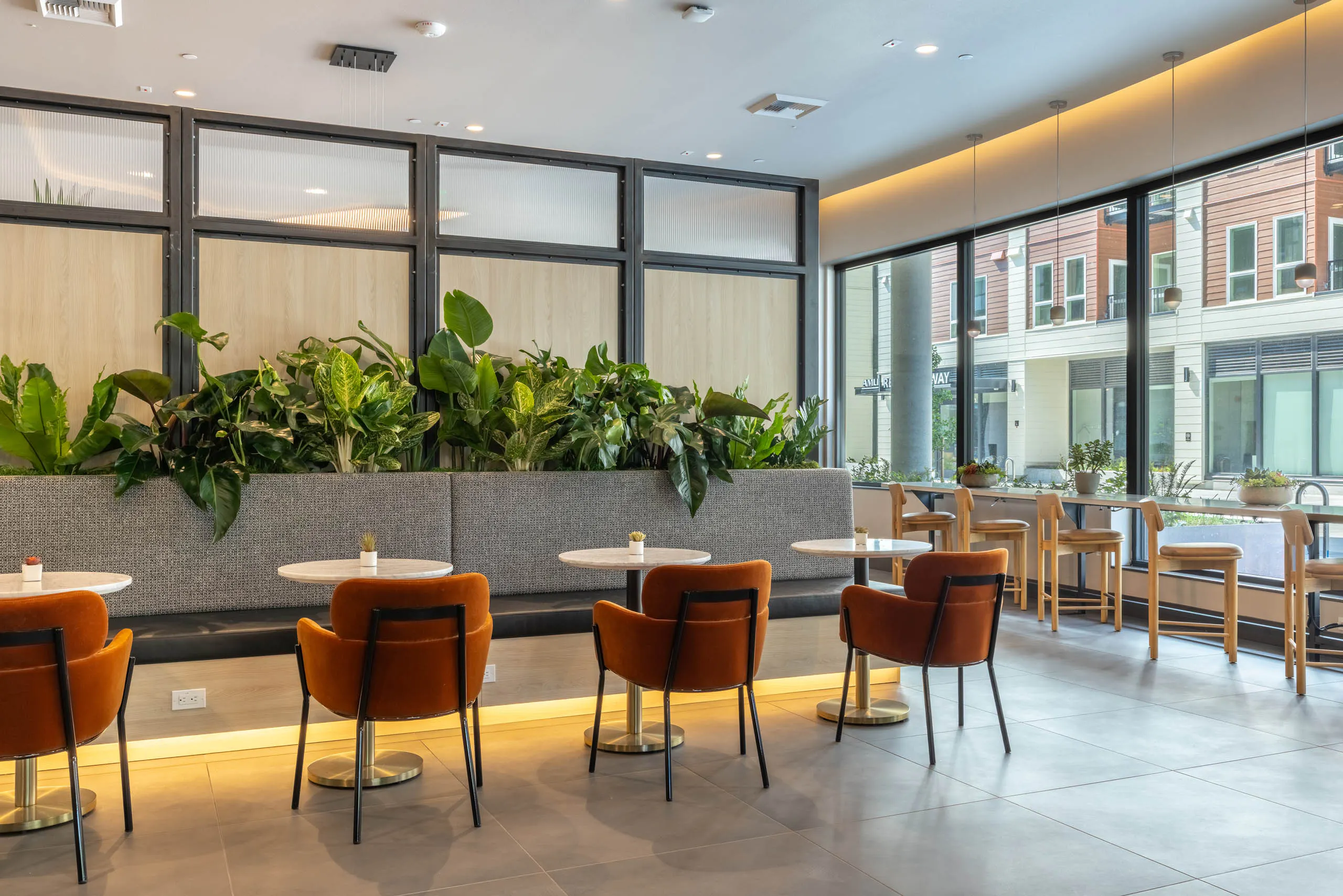 East Building lobby seating area with bistro tables, orange chairs, greenery, and large windows.