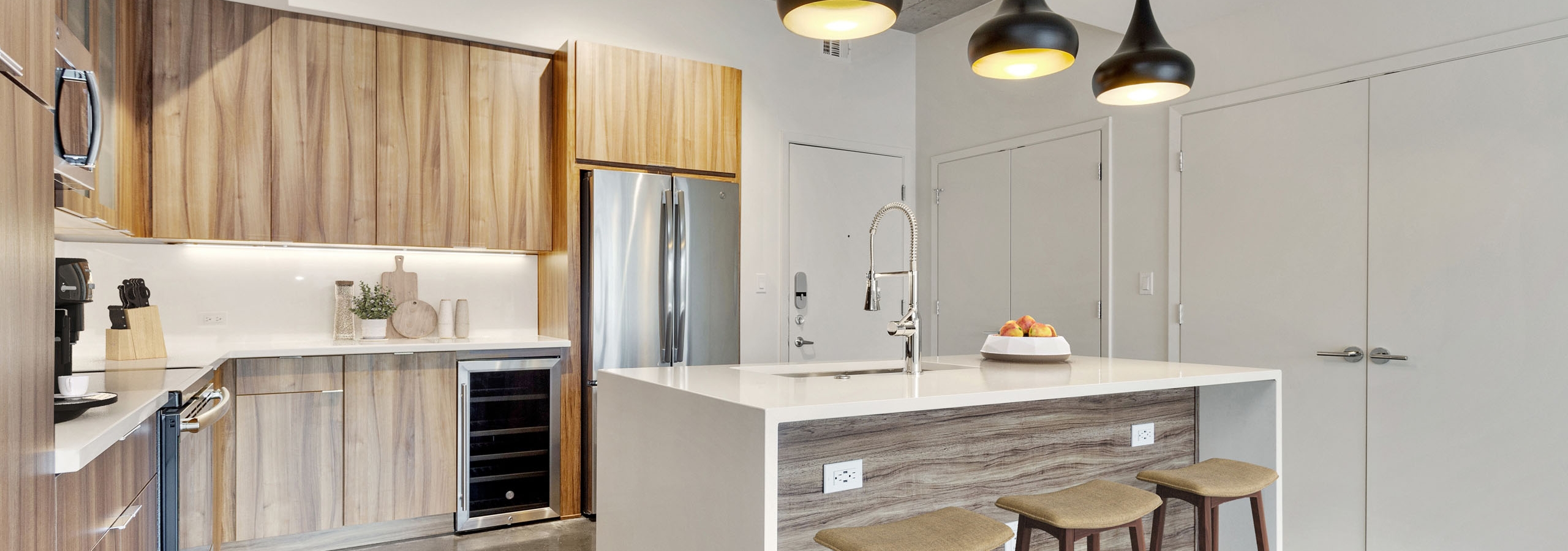 Interior view of kitchen with wood cabinets and a white quartz island with three black pendant lights above at AMLI on 2nd