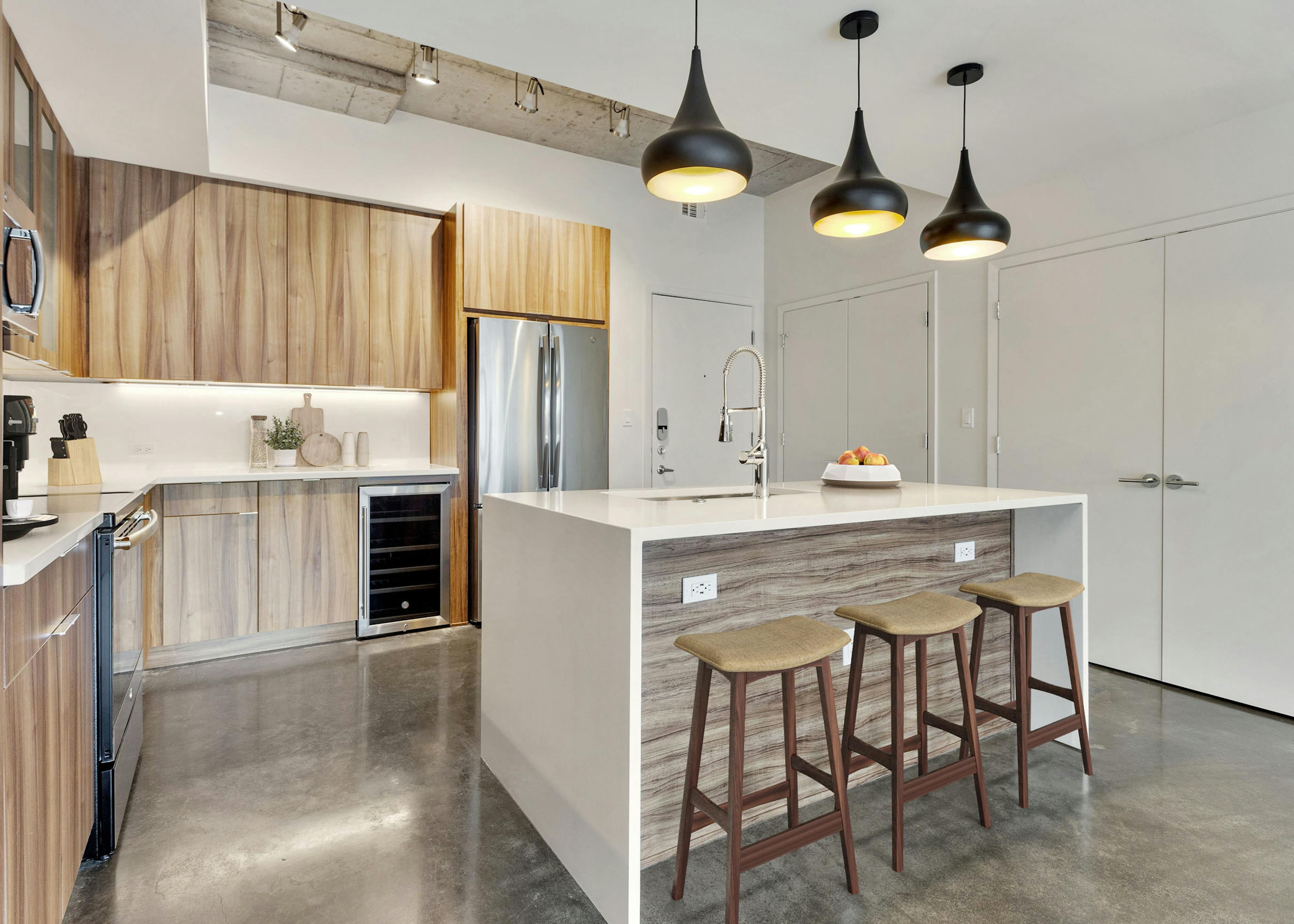 Interior view of kitchen with wood cabinets and a white quartz island with three black pendant lights above at AMLI on 2nd