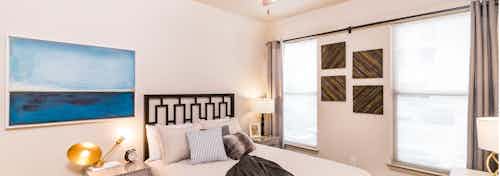 Interior view of a bedroom at AMLI Inverness with a bed with black metal headboard and a blue painting on the wall and lamps