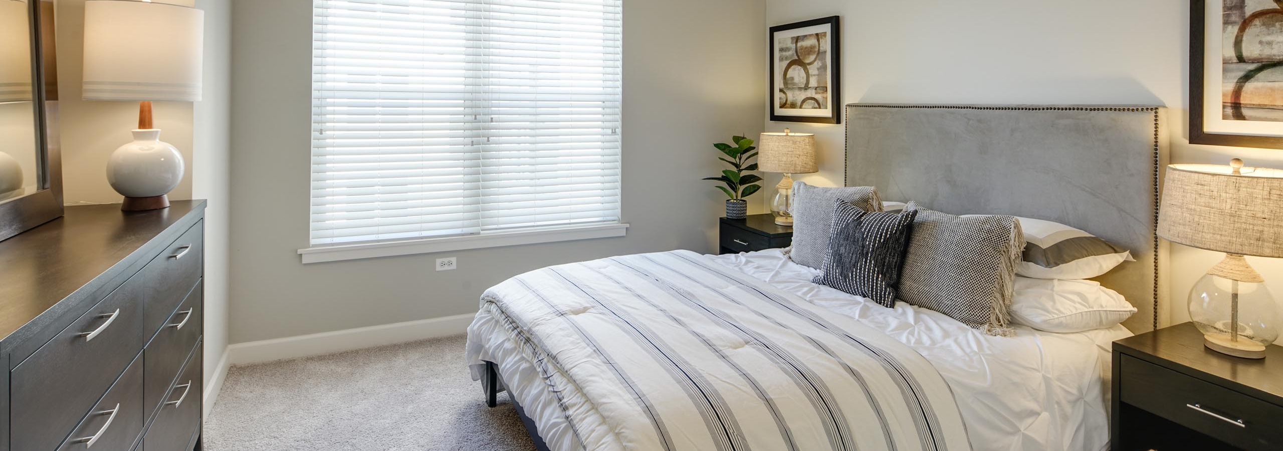 AMLI Evanston apartment bedroom with grey walls and carpet flooring featuring dark wood furniture and neutral striped bedding