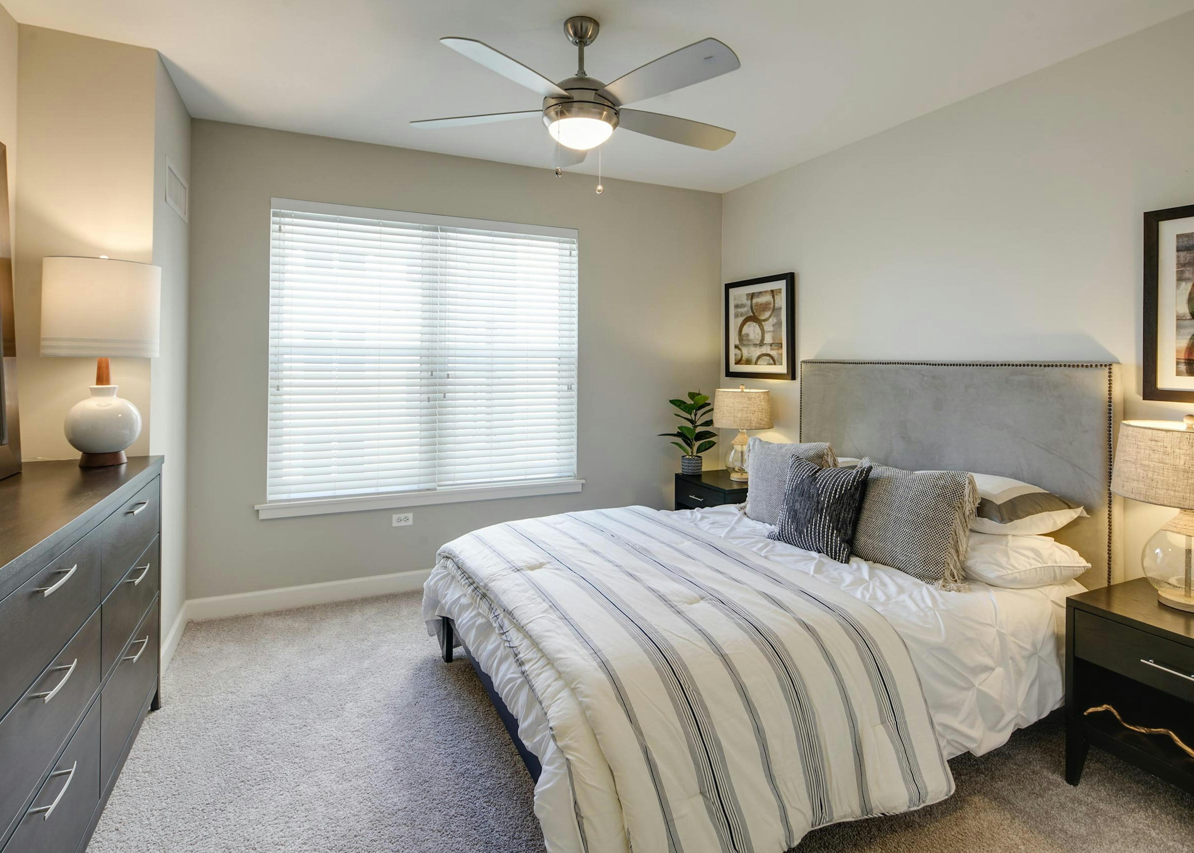 AMLI Evanston apartment bedroom with grey walls and carpet flooring featuring dark wood furniture and neutral striped bedding