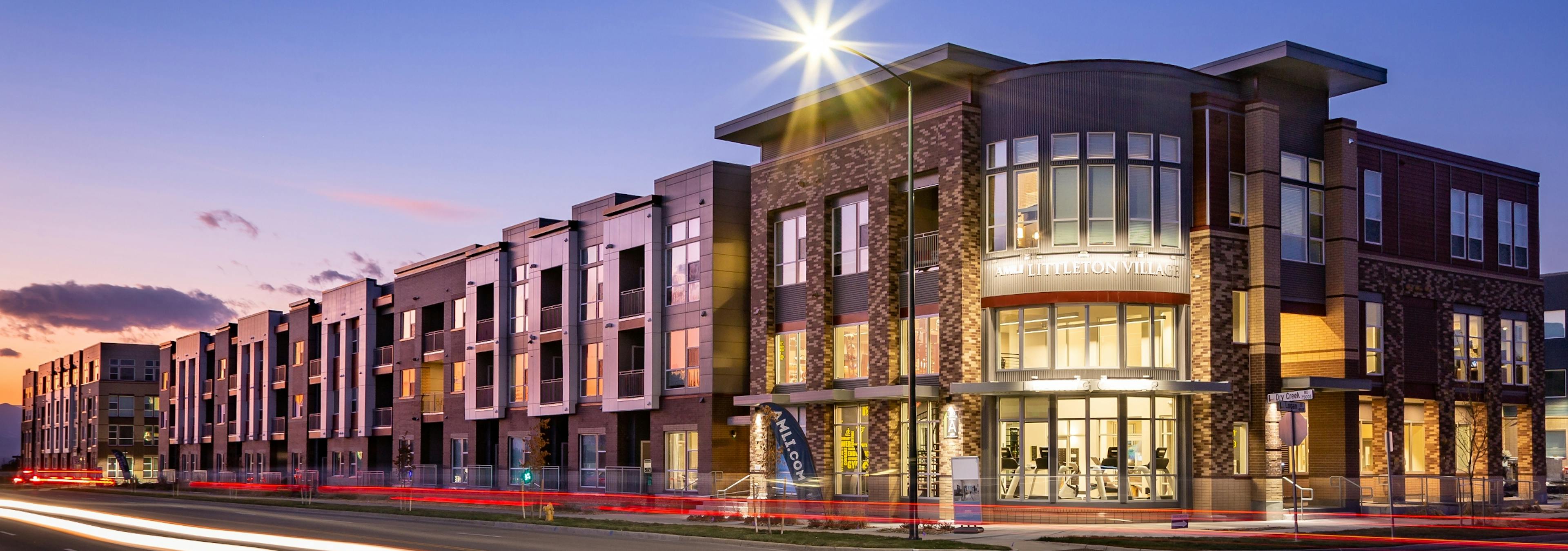 Exterior dusk rendering of AMLI Littleton Village apartment building’s brick facade and entrance with lit monument sign 