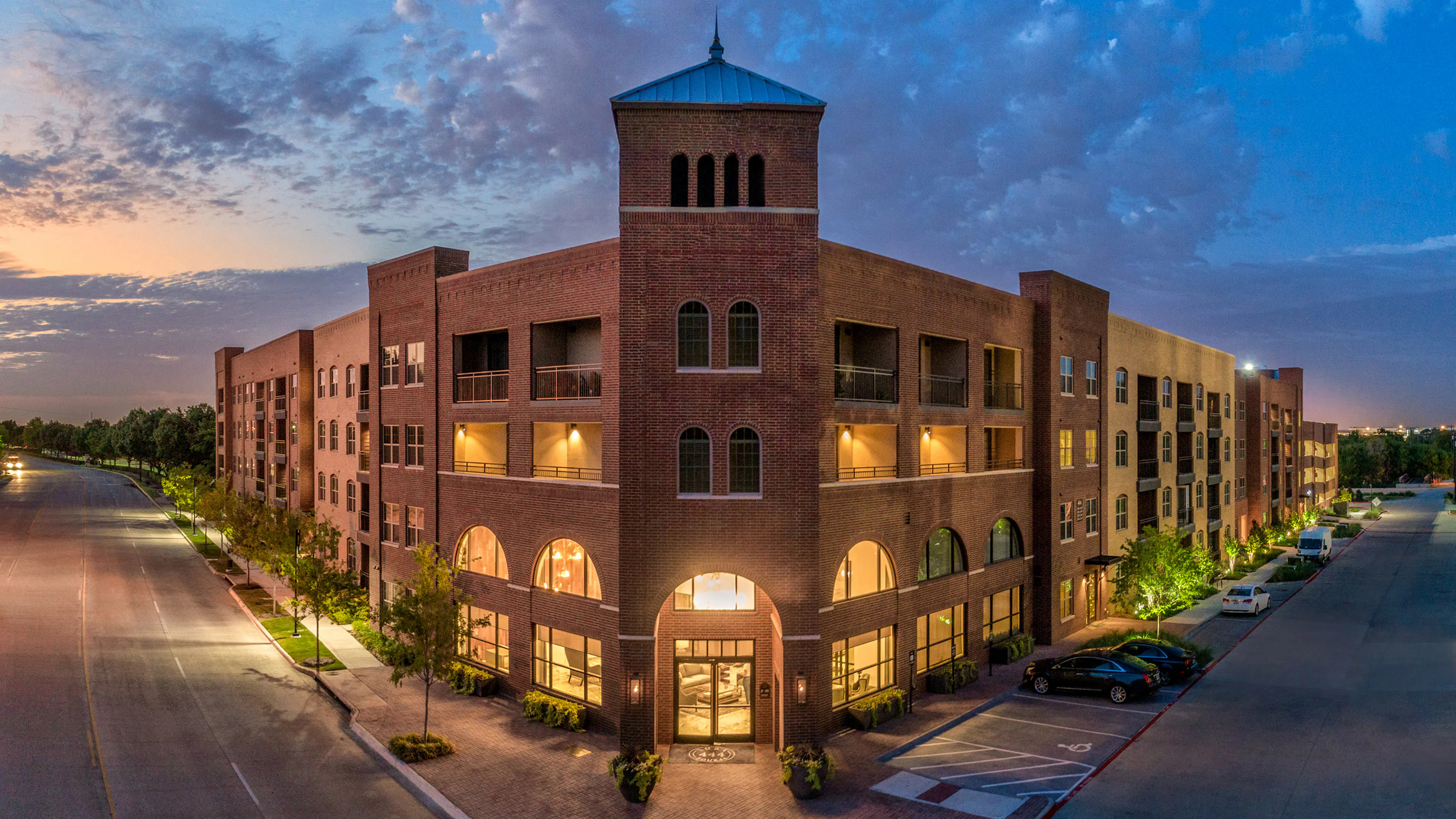 Evening view of the AMLI Grapevine apartment building with illuminated windows and a dark blue sky with scattered clouds
