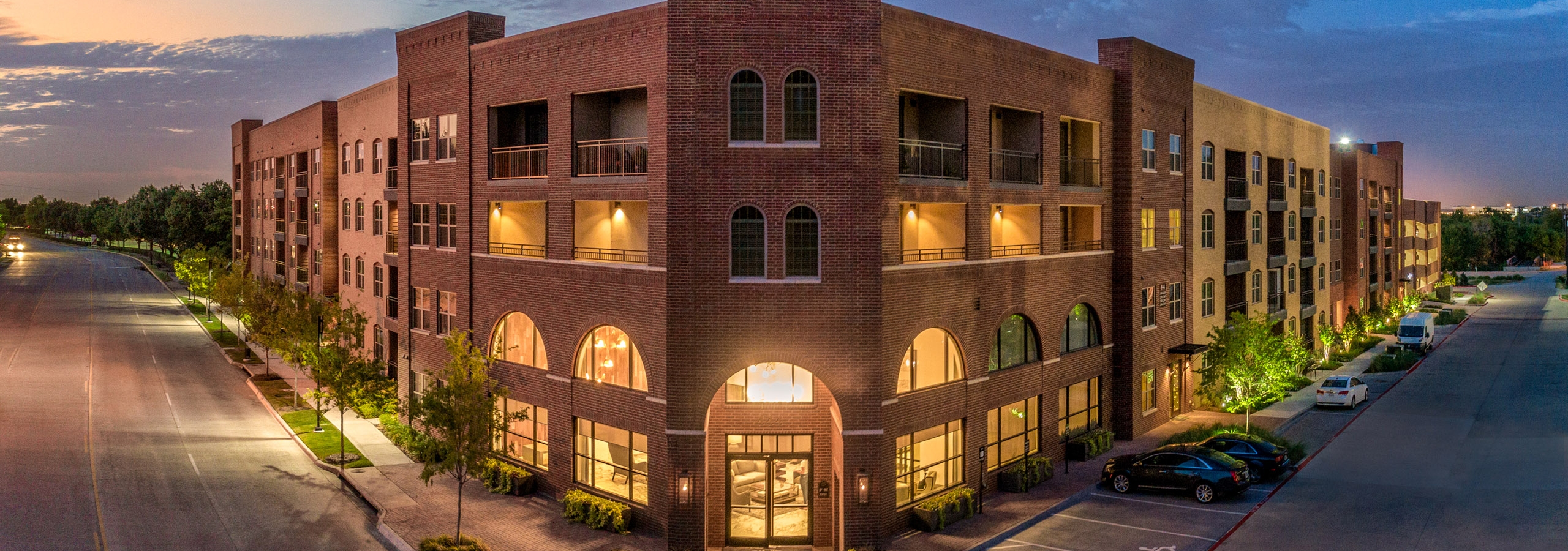 Evening view of the AMLI Grapevine apartment building with illuminated windows and a dark blue sky with scattered clouds