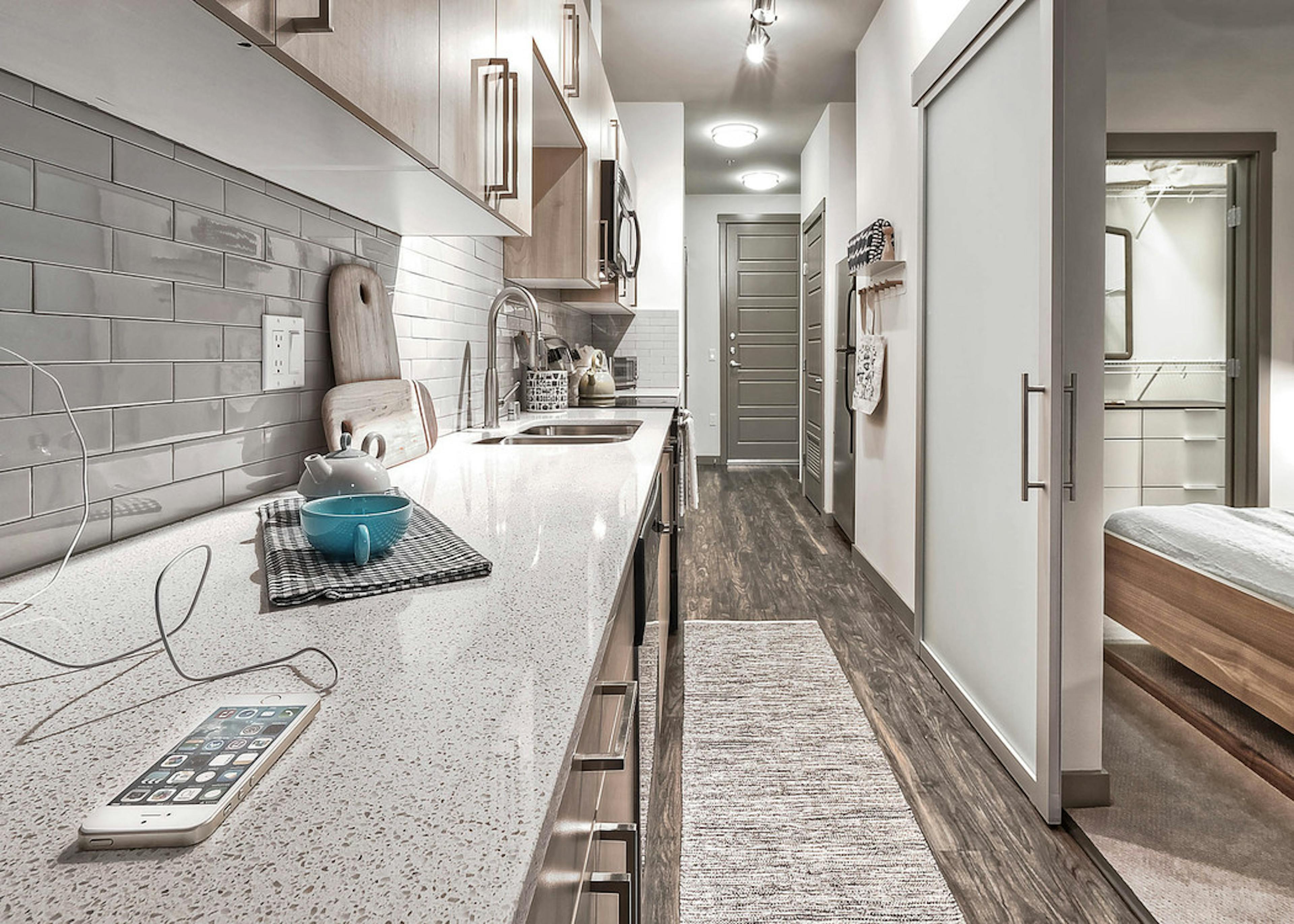 Interior view of AMLI Mark24 apartment kitchen with light cabinets white quartz counter tops and grey back splash  