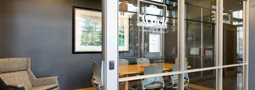 AMLI on 2nd conference room with glass walls and long wooden desk with grey office chairs and beige lounge chair to the left
