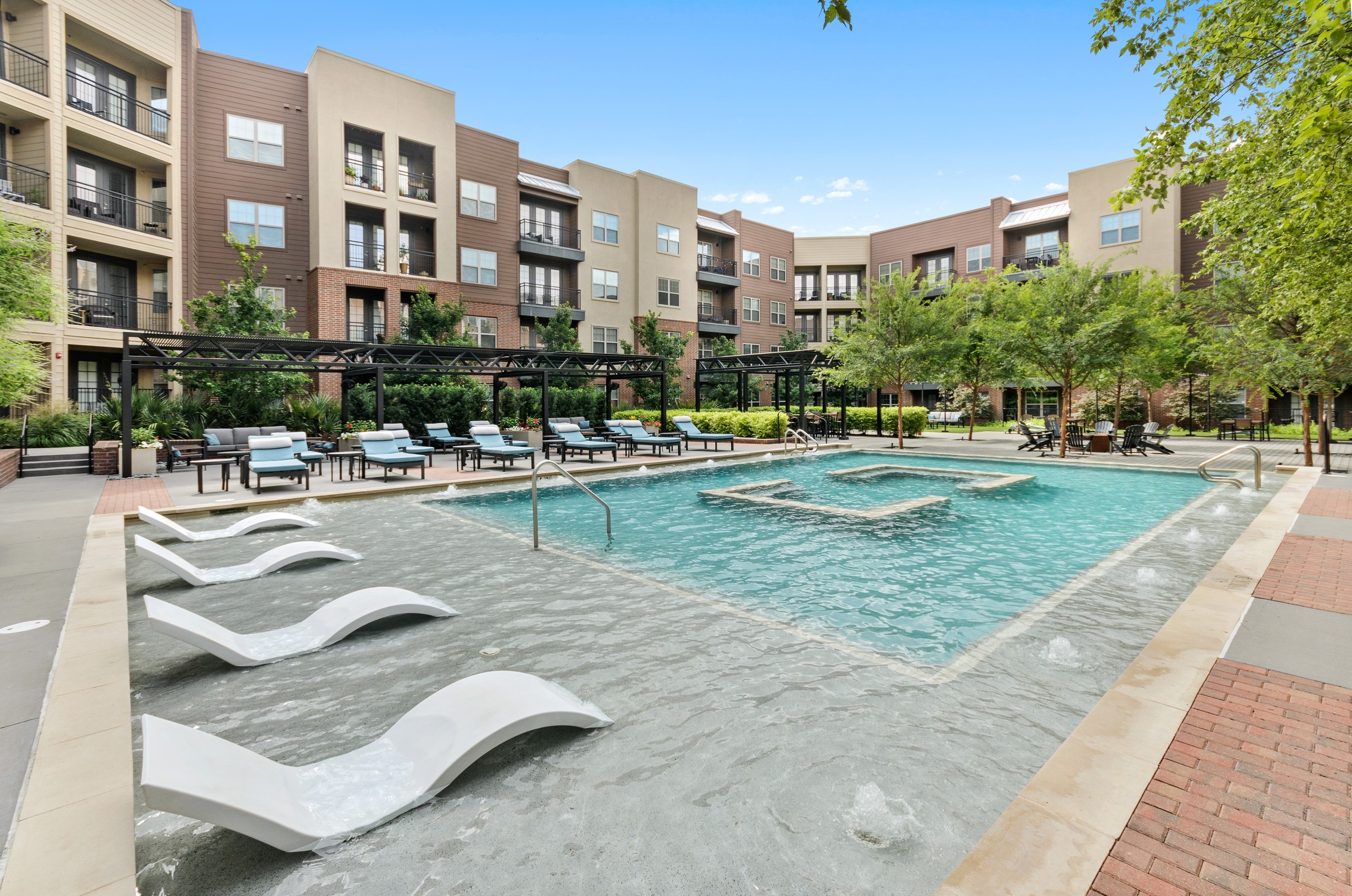 AMLI Grapevine courtyard pool with blue and white lounge chairs and poolside deck with a firepit shaded by trees