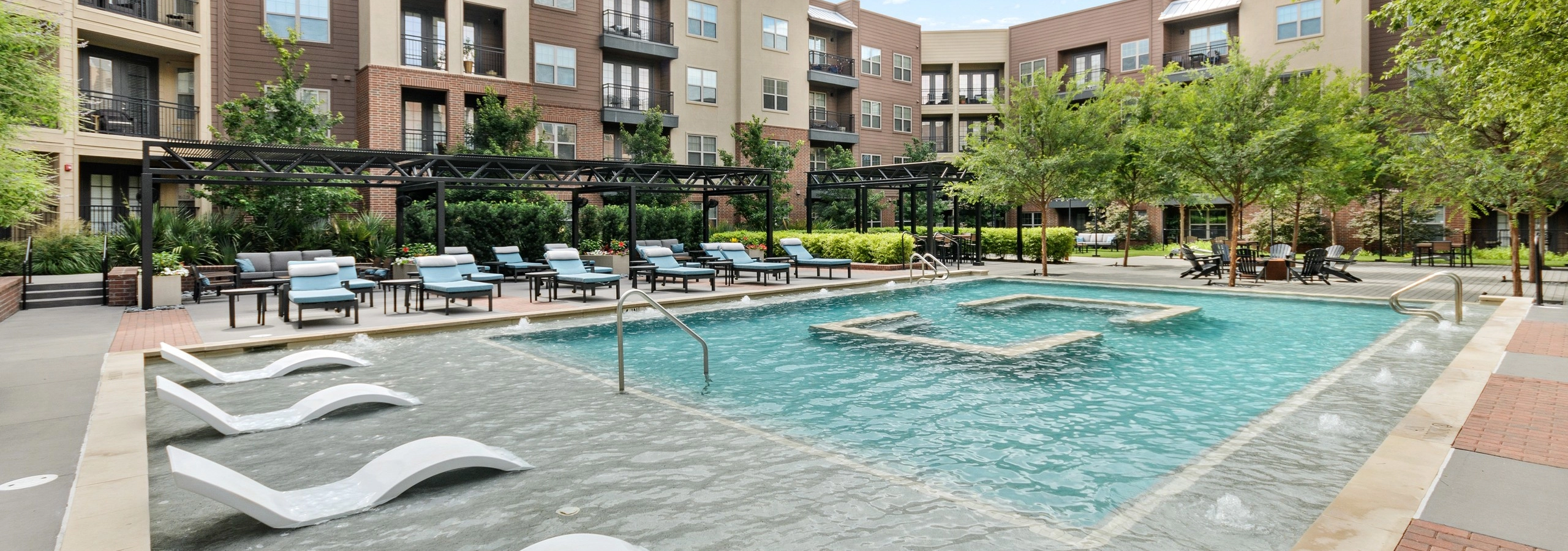 AMLI Grapevine courtyard pool with blue and white lounge chairs and poolside deck with a firepit shaded by trees