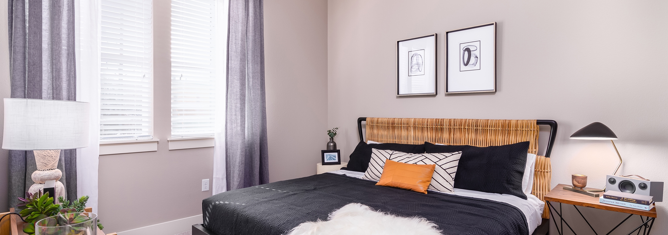 Interior view of AMLI Littleton Village apartment bedroom with king bed with wicker headboard and curtains over large window