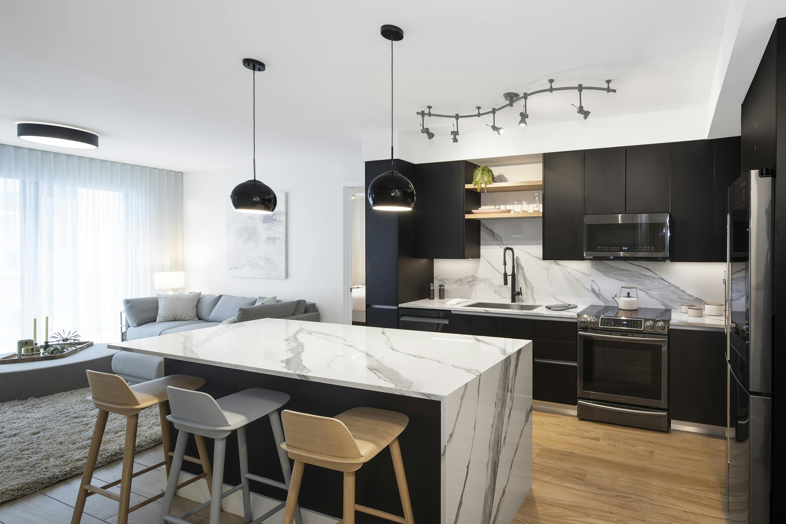 Interior view of AMLI Midtown Miami apartment kitchen with center marble island and modern appliances and living area at left