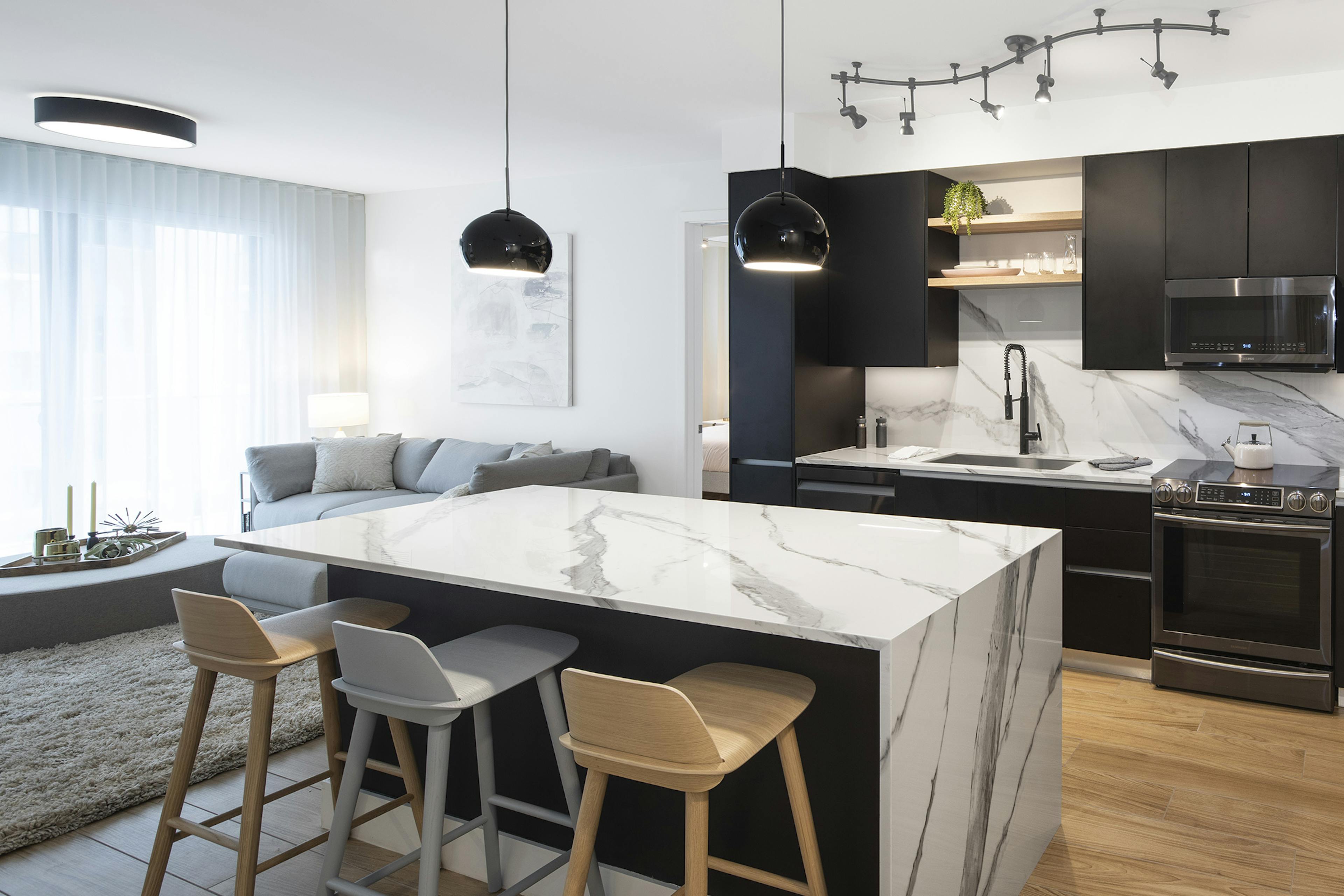 Interior view of AMLI Midtown Miami apartment kitchen with center marble island and modern appliances and living area at left
