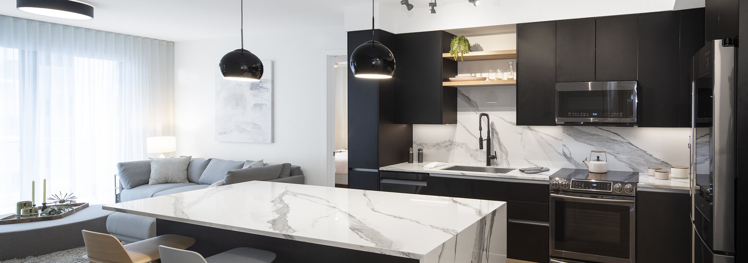 Interior view of AMLI Midtown Miami apartment kitchen with center marble island and modern appliances and living area at left