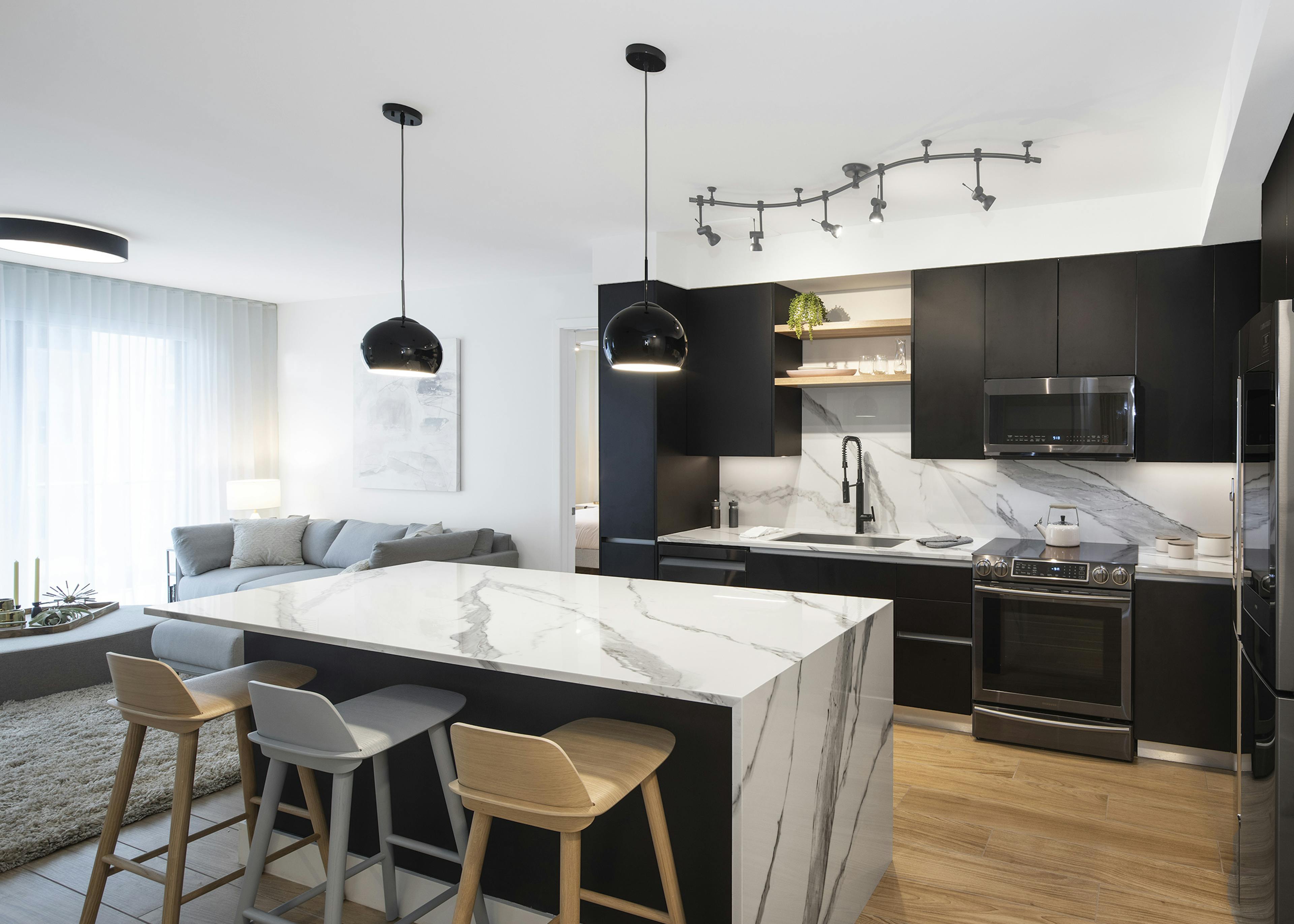 Interior view of AMLI Midtown Miami apartment kitchen with center marble island and modern appliances and living area at left