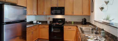 View of a spacious AMLI 900 apartment kitchen with maple cabinets and granite countertops paired with black appliances