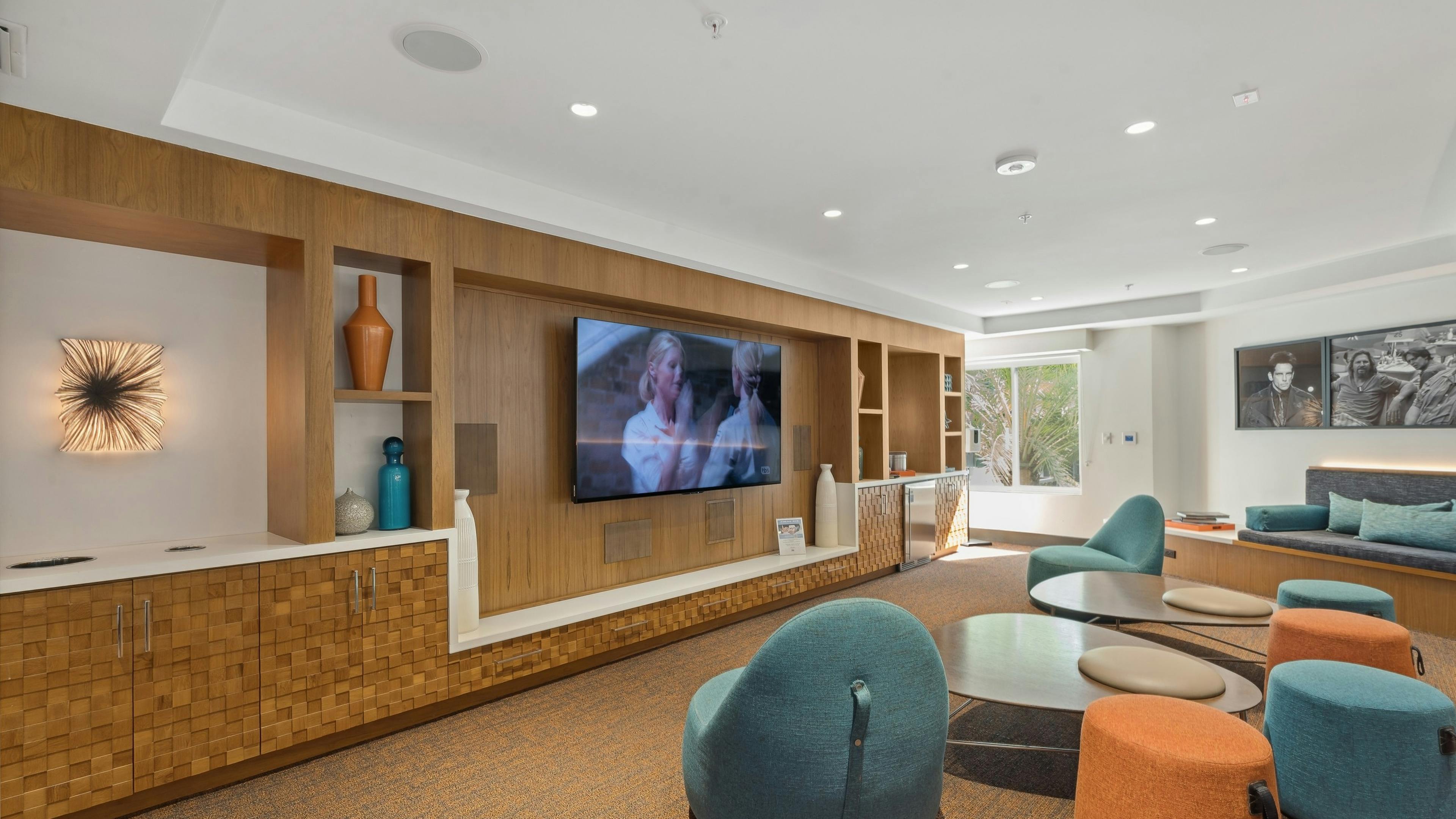 Media lounge at AMLI Uptown Orange with colorful lounge seating facing a big screen TV on wood wall with shelves