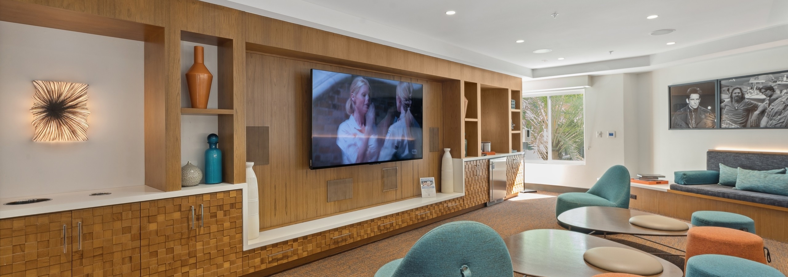 Media lounge at AMLI Uptown Orange with colorful lounge seating facing a big screen TV on wood wall with shelves