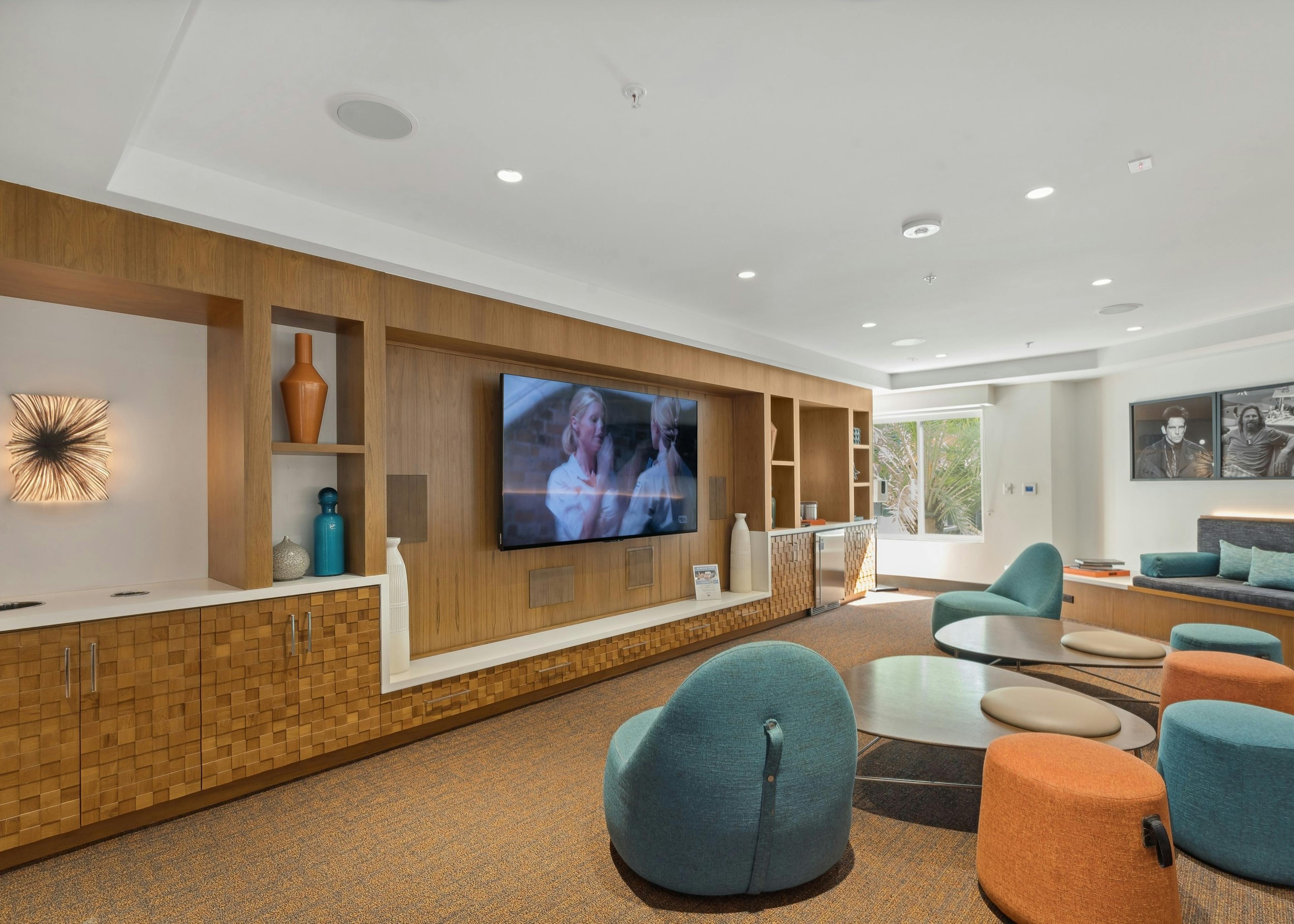 Media lounge at AMLI Uptown Orange with colorful lounge seating facing a big screen TV on wood wall with shelves
