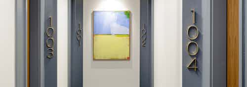 Hallway at AMLI Fountain Place apartment building with 4 apartment doorways with blue and yellow painting at end of hall