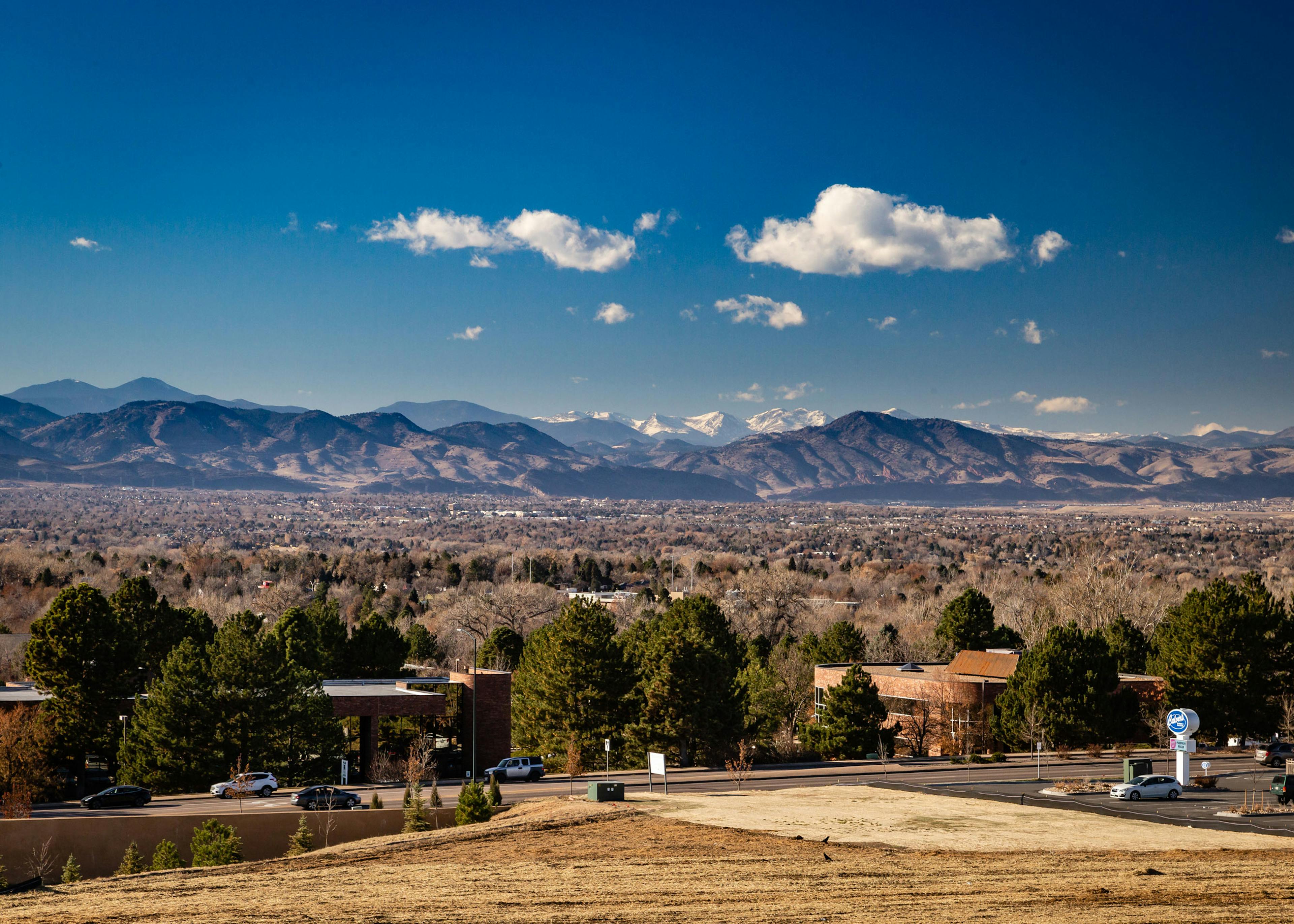 Daytime aerial view above AMLI Littleton Village apartments with the Rocky Mountains from afar, blue sky and lush greenery