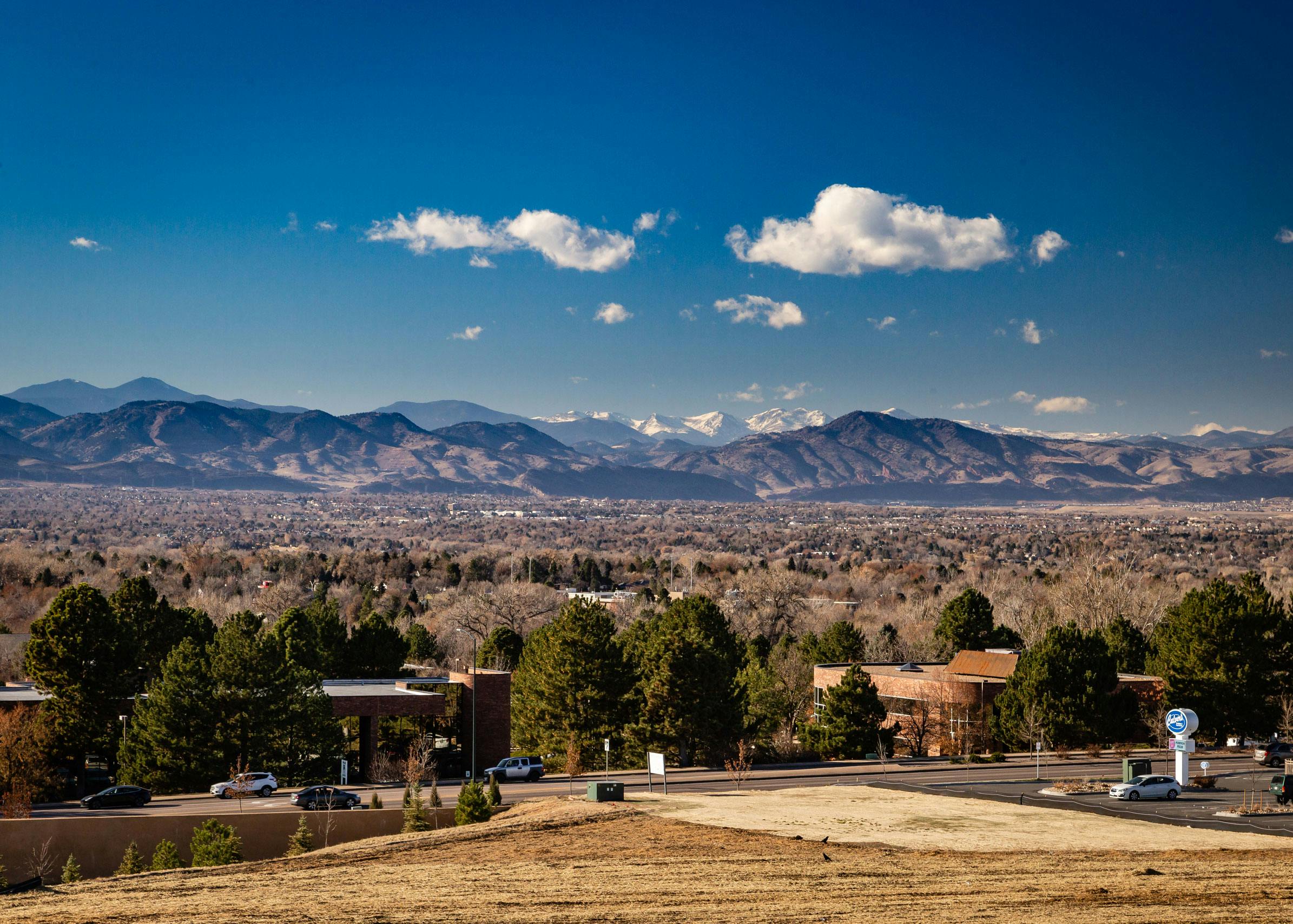 Daytime aerial view above AMLI Littleton Village apartments with the Rocky Mountains from afar, blue sky and lush greenery
