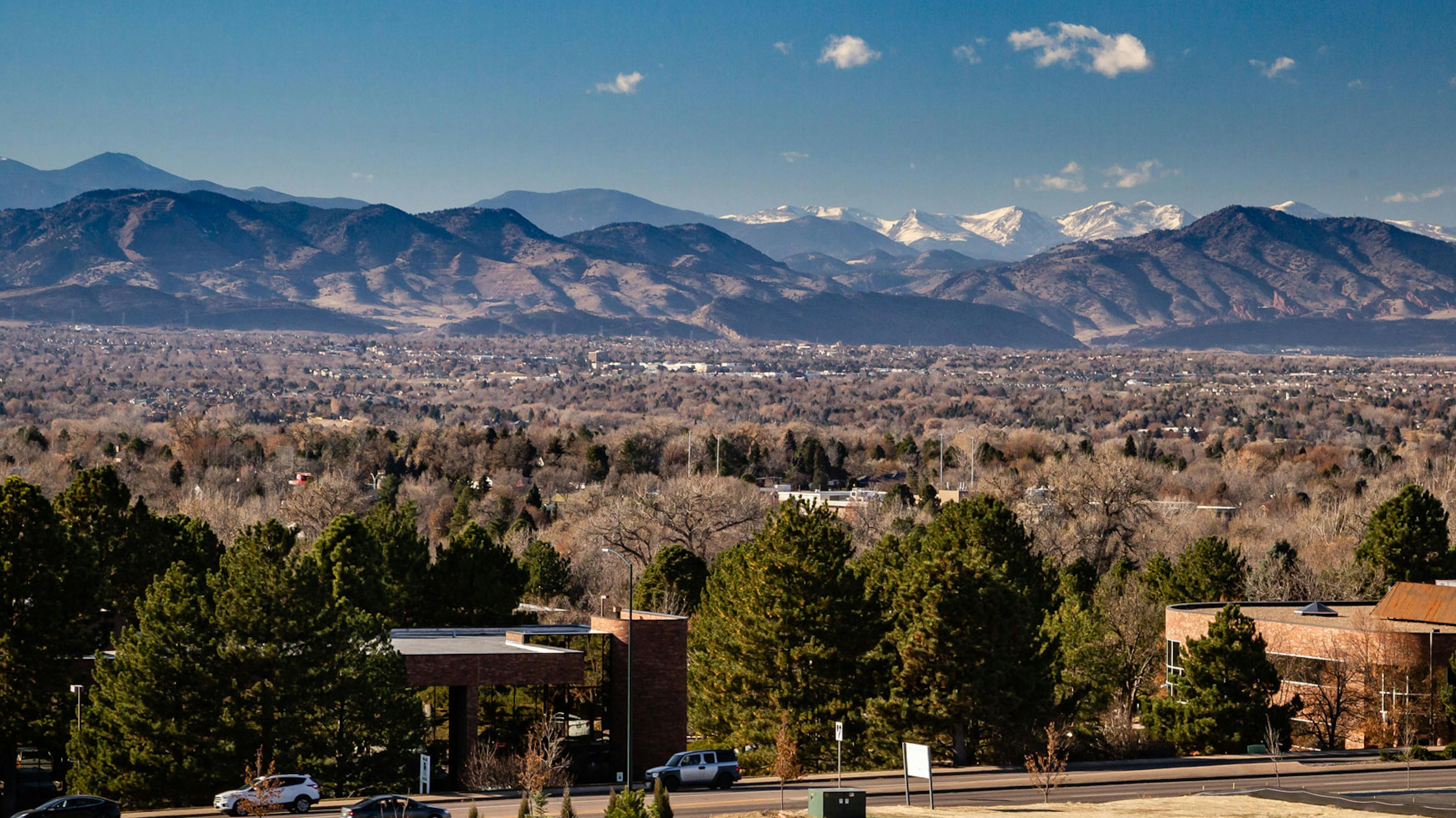 Daytime aerial view above AMLI Littleton Village apartments with the Rocky Mountains from afar, blue sky and lush greenery