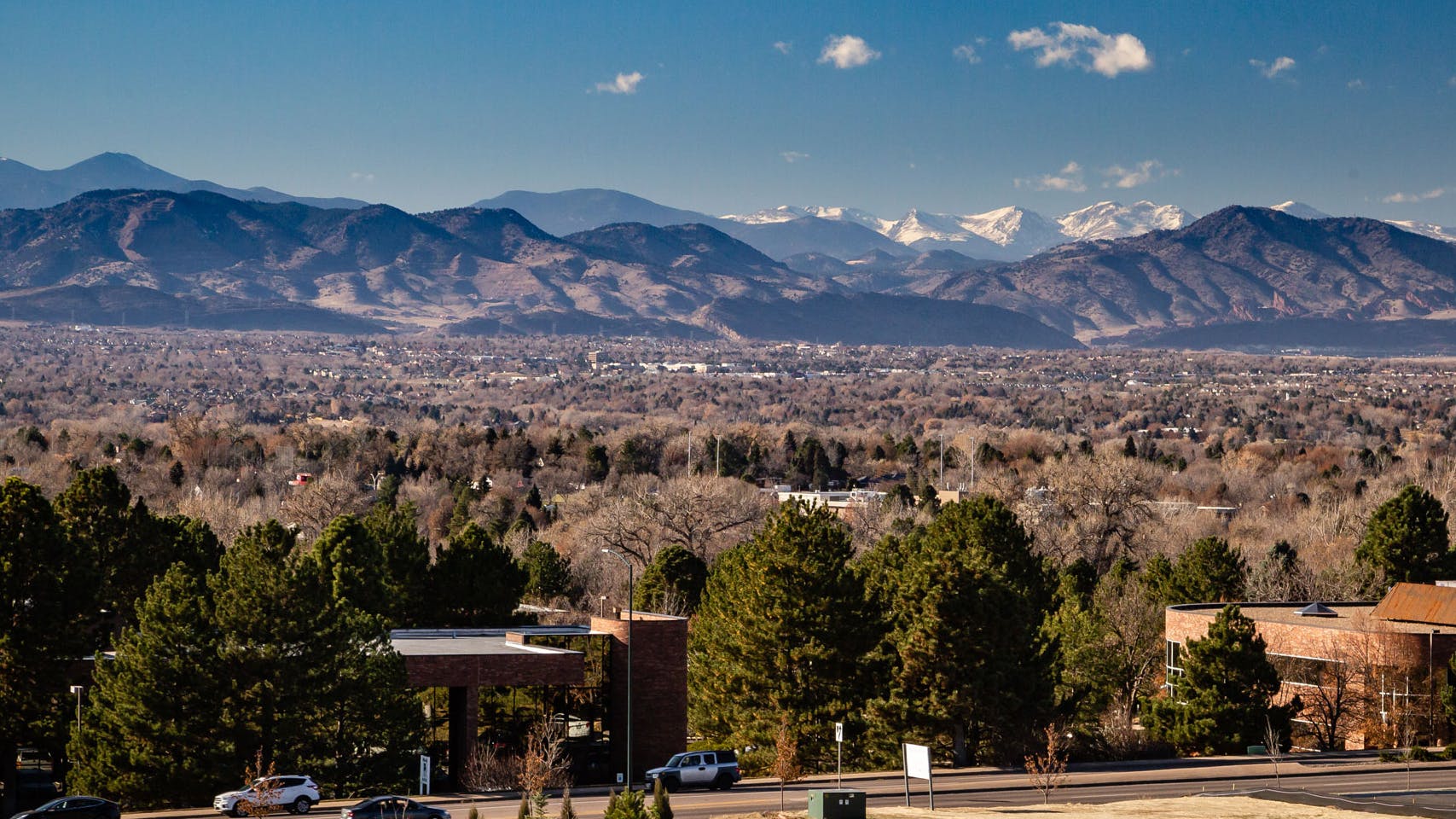 Daytime aerial view above AMLI Littleton Village apartments with the Rocky Mountains from afar, blue sky and lush greenery
