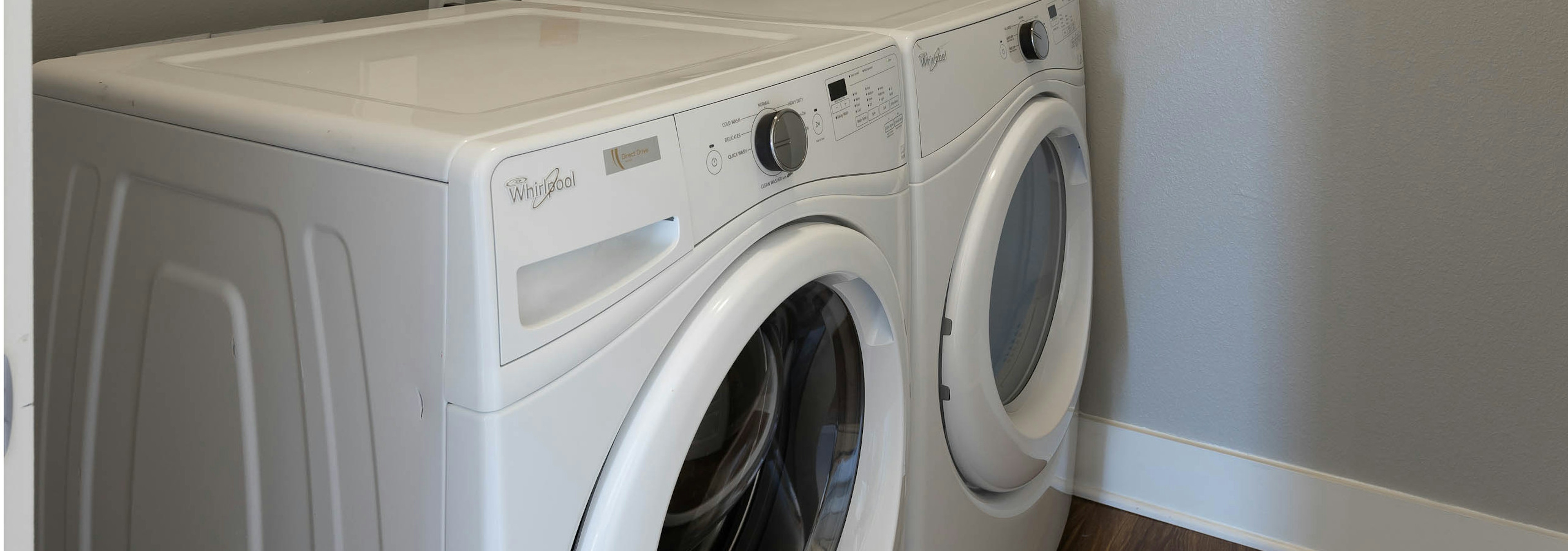 Close up view of in unit white washer and dryer set at AMLI on Aldrich apartment community with white trim and light walls