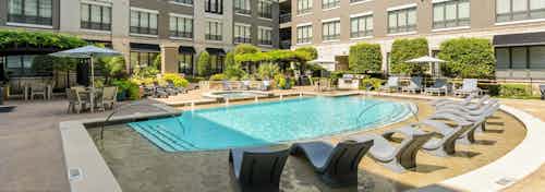 Large courtyard pool at AMLI Las Colinas apartments with in pool lounges and surrounding seating and lush landscaping