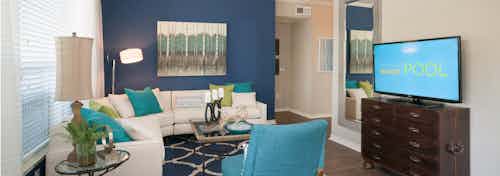 Interior of apartment living room at AMLI Memorial Heights with white sectional couch on dark blue wall and TV on chest