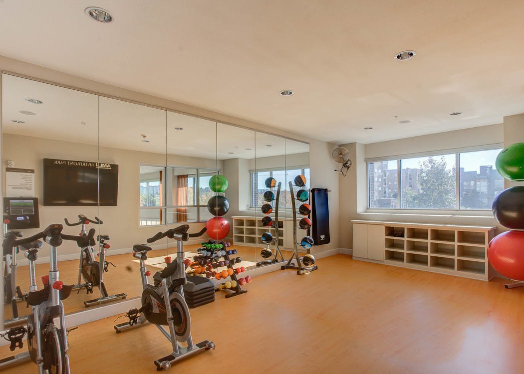A yoga studio at AMLI Riverfront Park apartments with a floor to ceiling mirror and stationary bikes and weights and windows