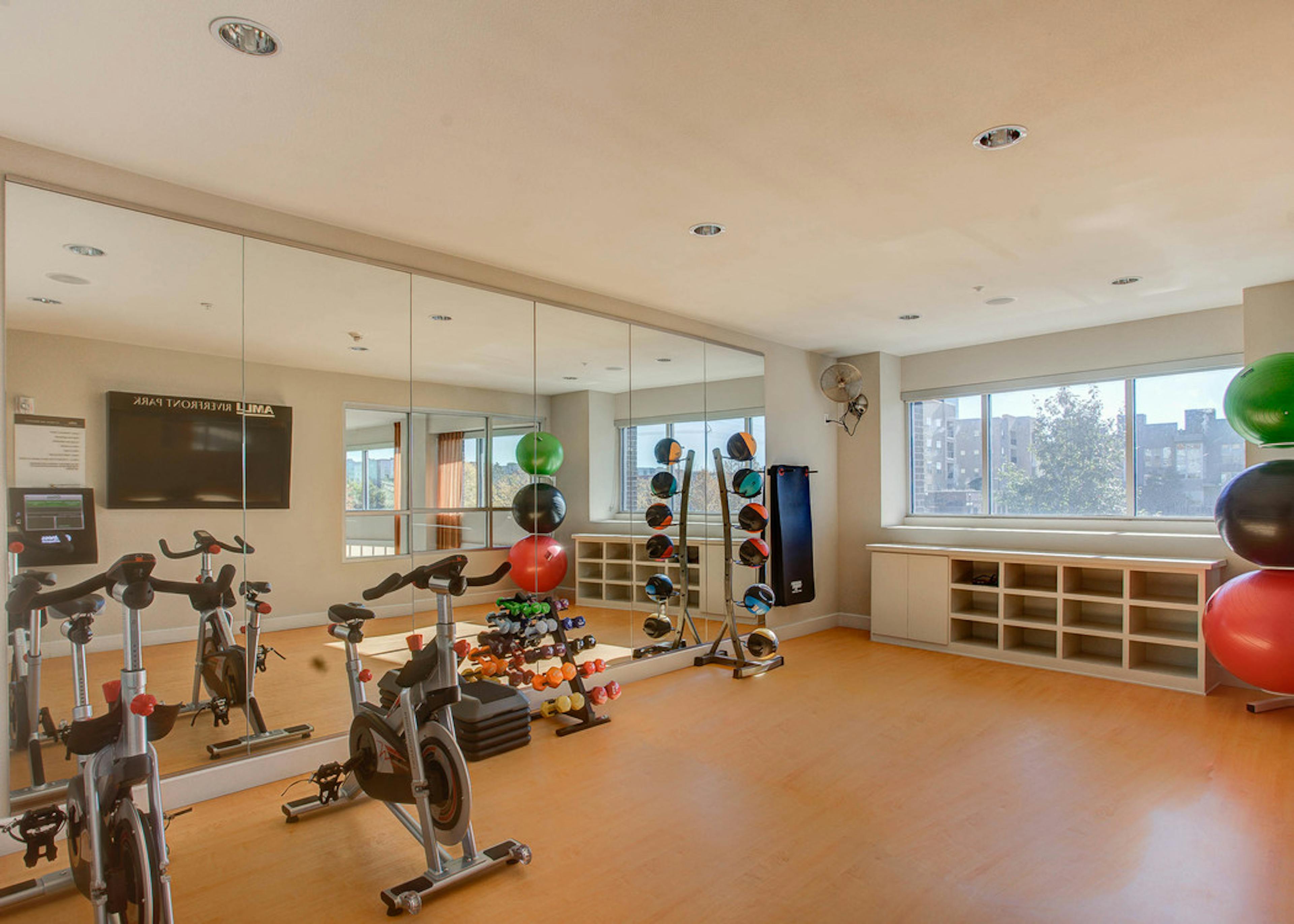 A yoga studio at AMLI Riverfront Park apartments with a floor to ceiling mirror and stationary bikes and weights and windows