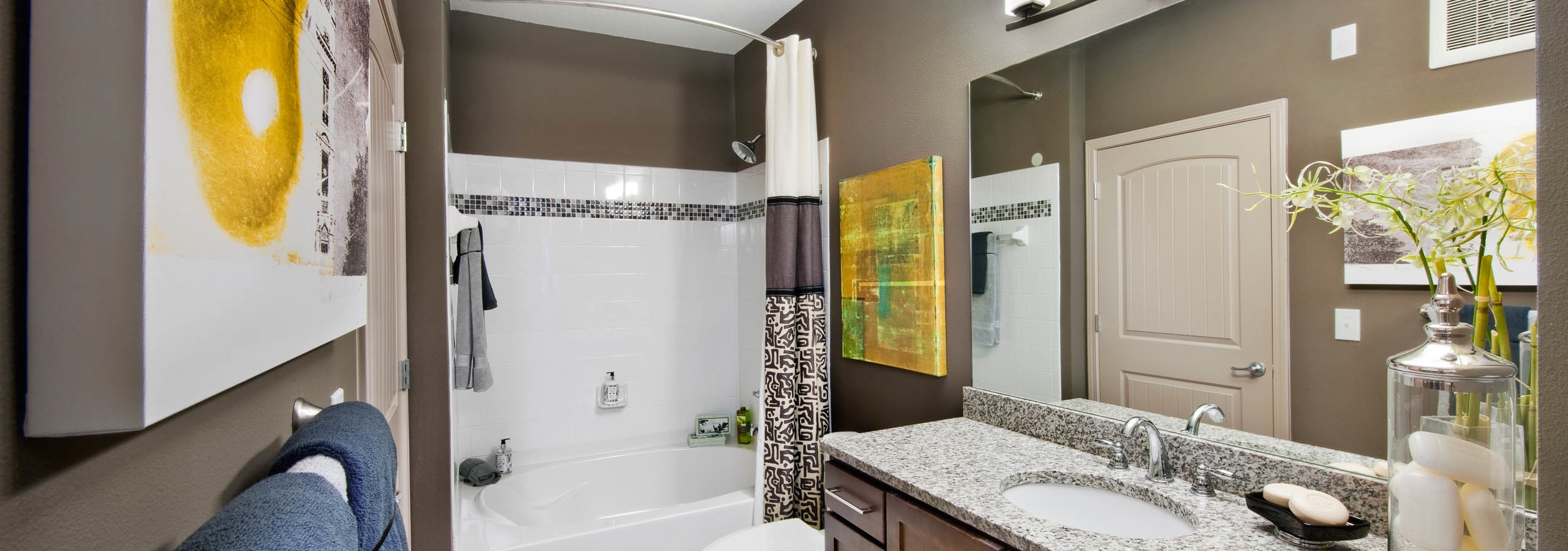 AMLI North Point bathroom with brown walls and white and yellow decor with a large vanity and white tiled bathtub