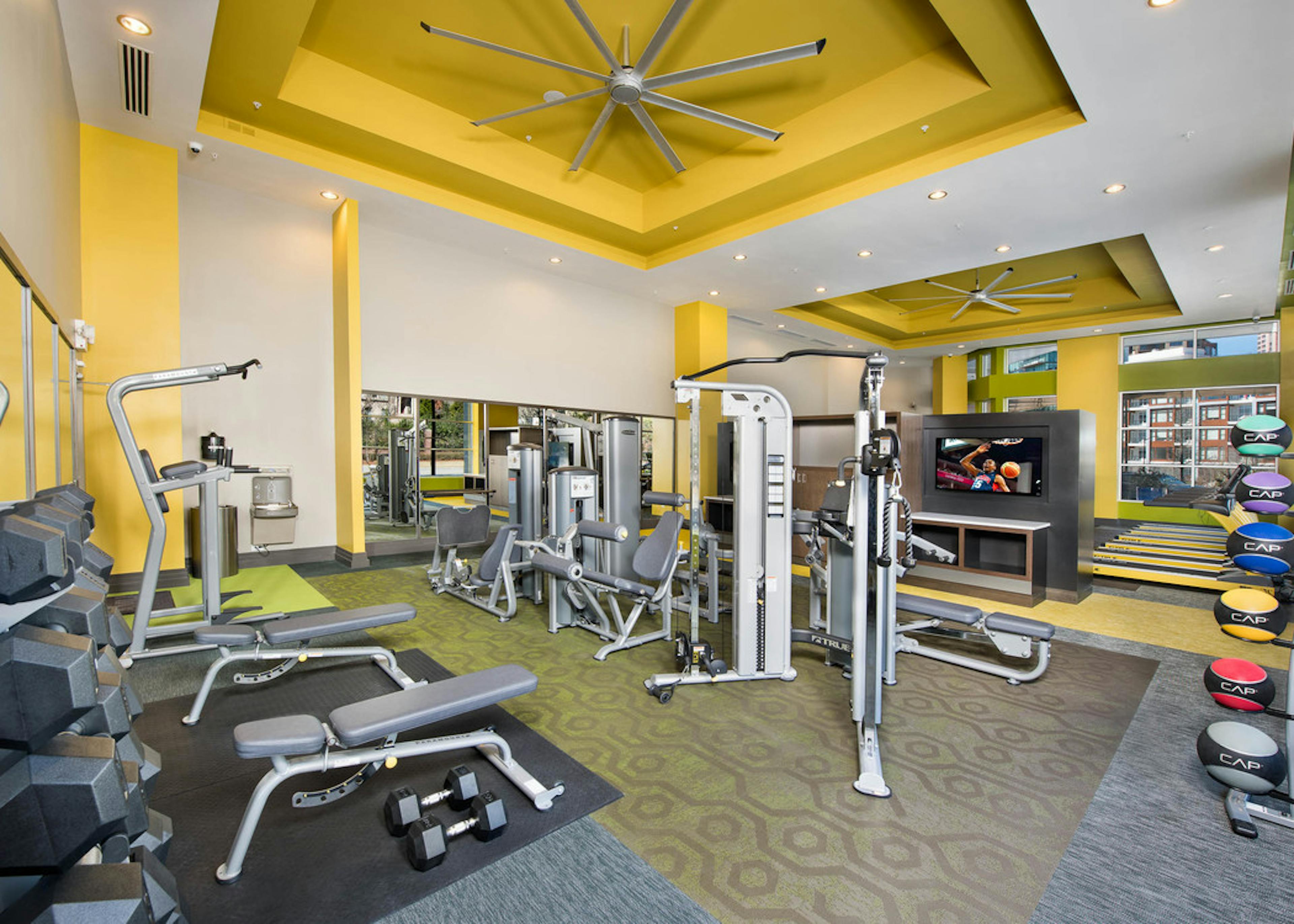 Interior of spacious AMLI Buckhead fitness center with a variety of weight machines with yellow walls and grey flooring