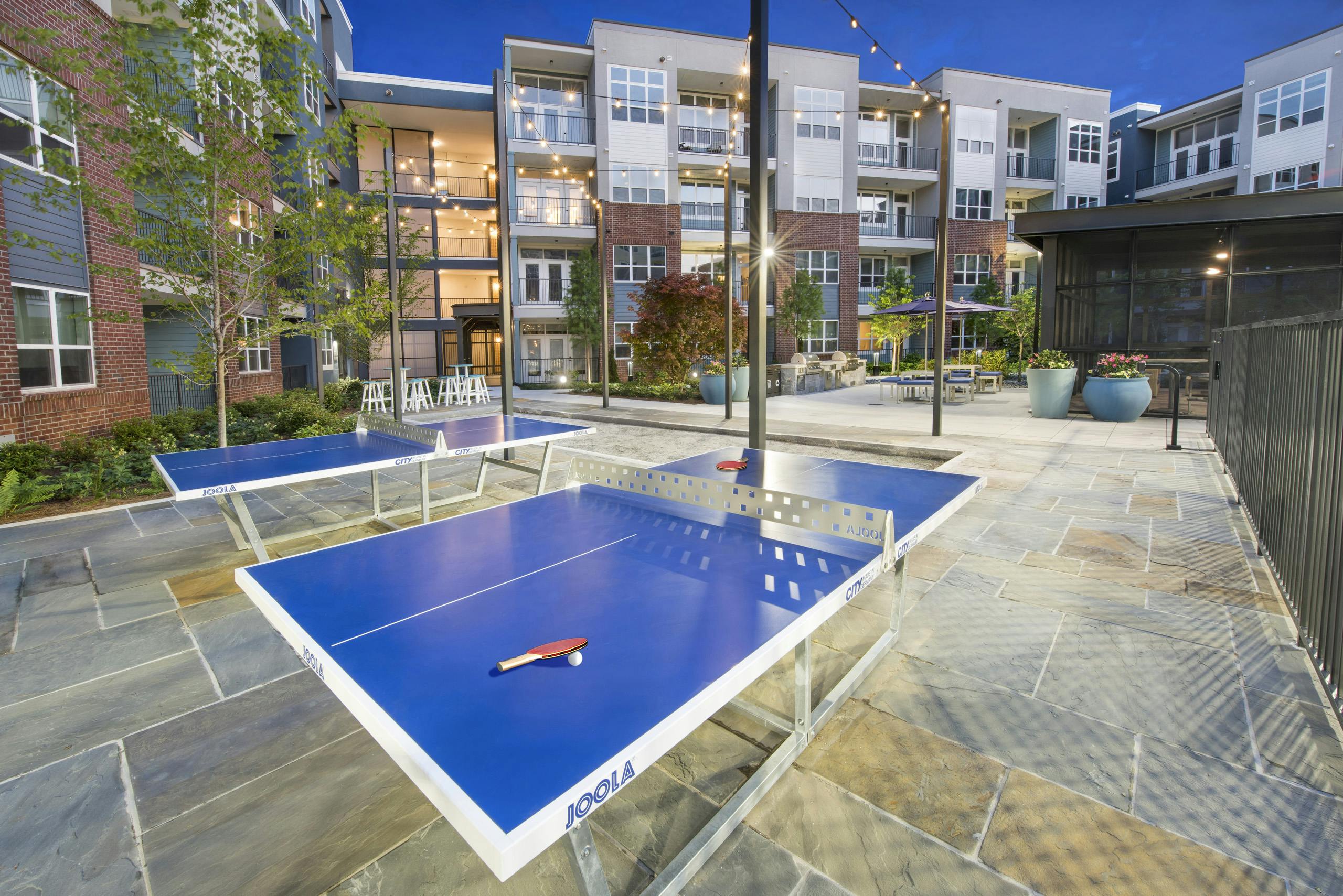Evening view of ping pong area at AMLI Decatur with blue ping pong tables and hanging lights with seating areas in the back